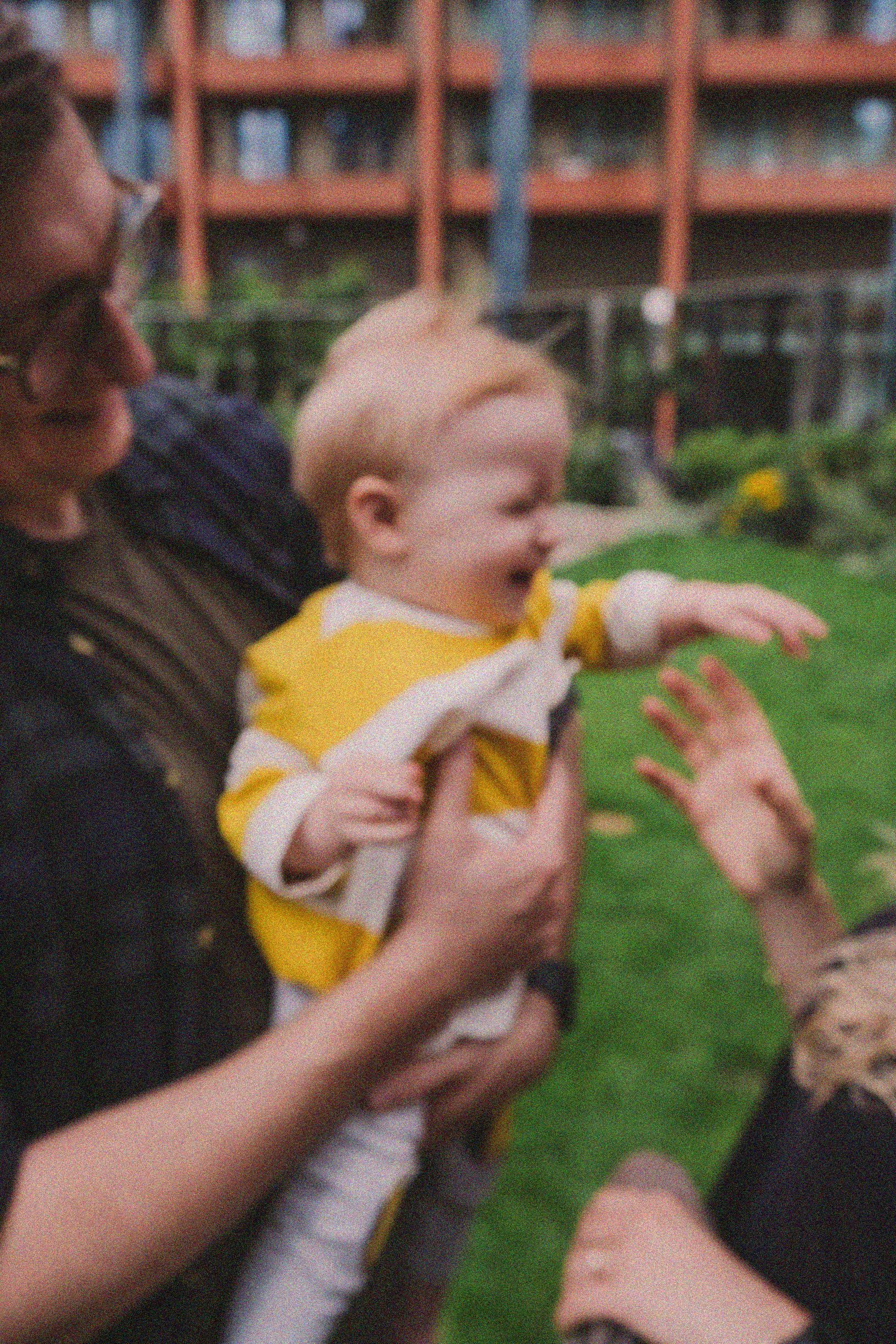 A small child in a yellow shirt being held and playing outdoors on a sunny day.