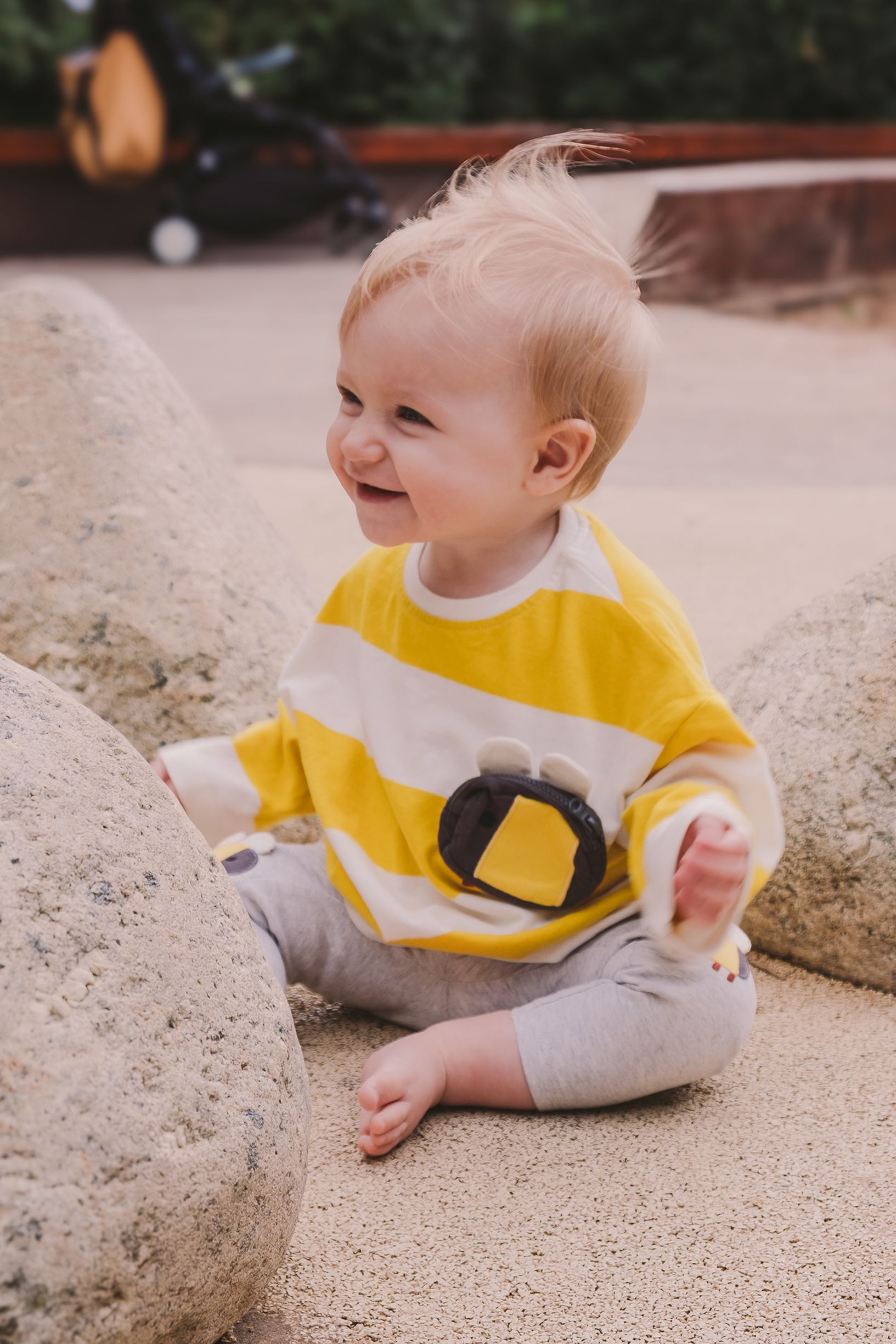 Baby wearing yellow and gray clothing sitting on textured ground.