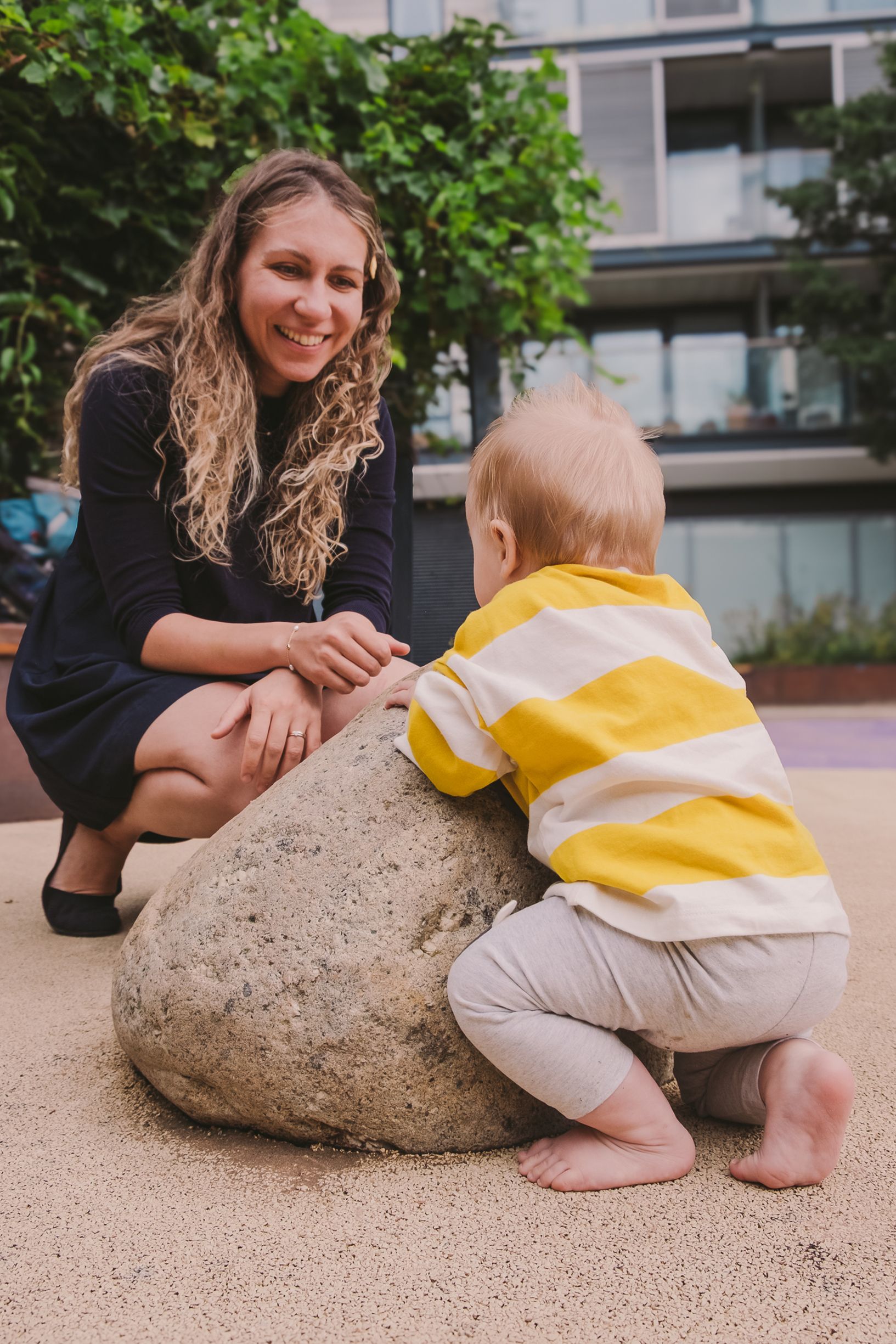 Baby in yellow and white outfit exploring a large rock outdoors.