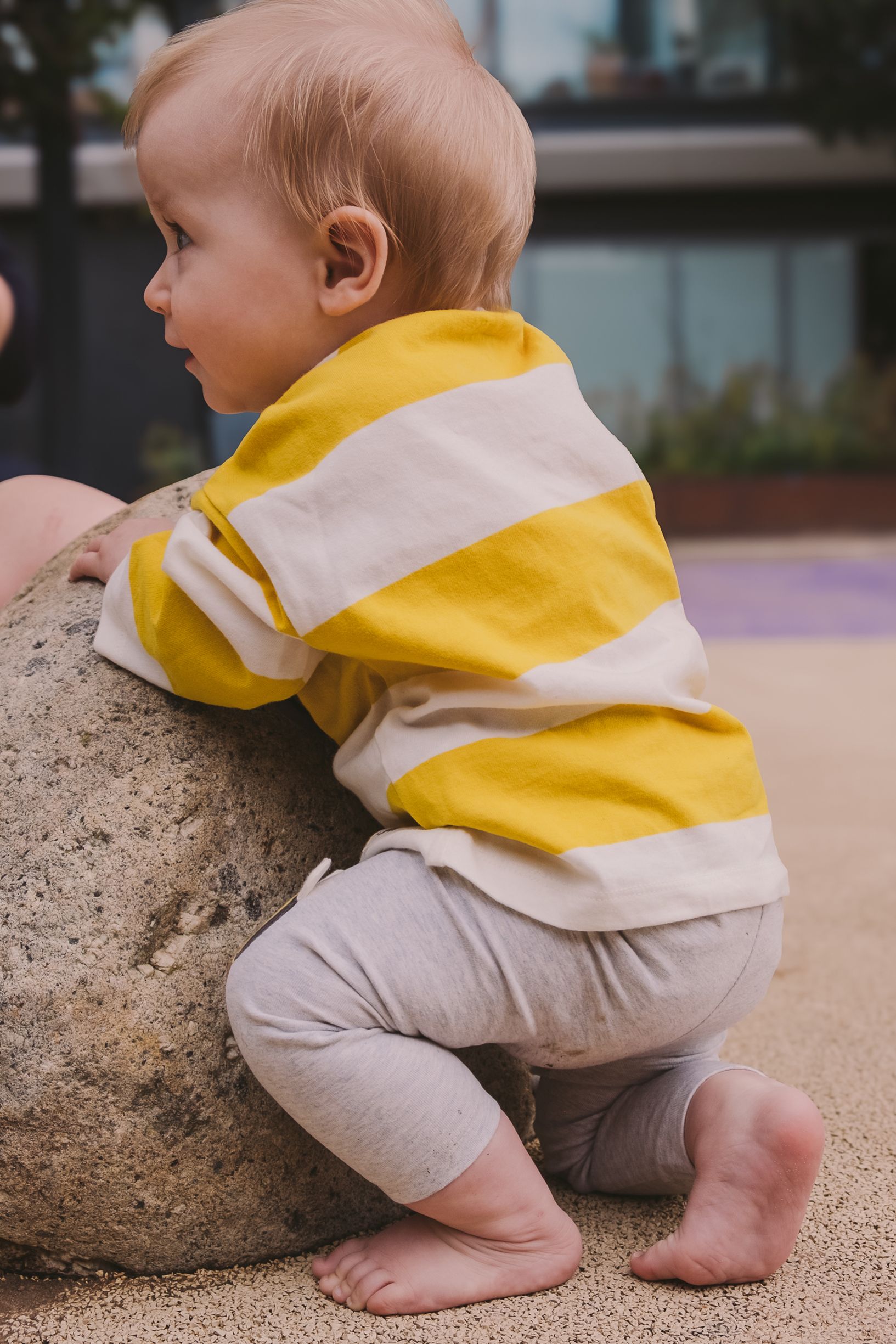 Baby in yellow striped clothing crawling near a large rock.