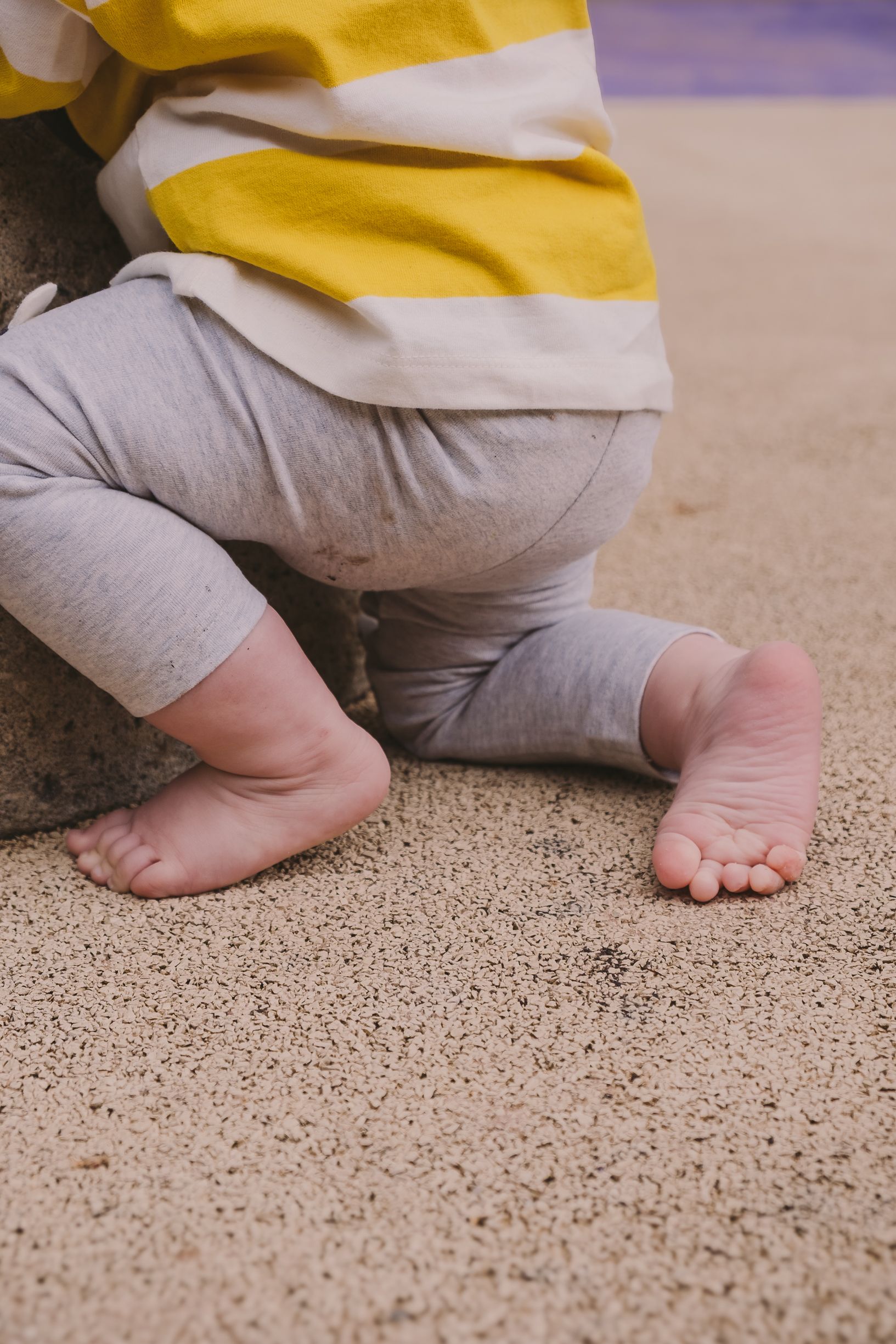 Close-up of baby feet and legs on textured ground.