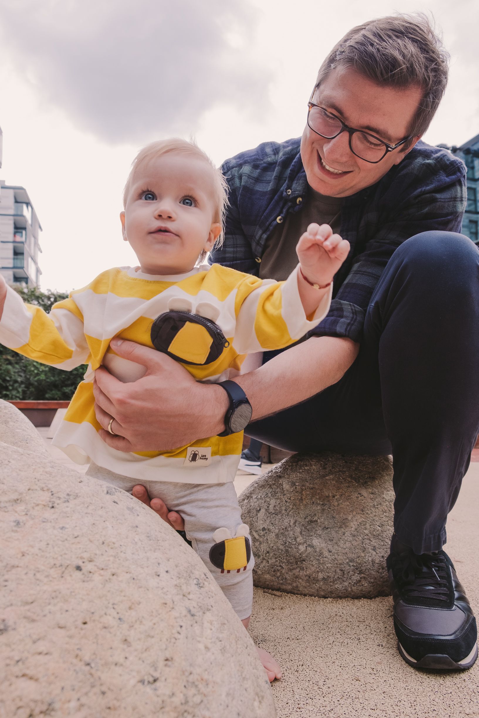 Baby in yellow shirt playing near a rock with adult supervision.