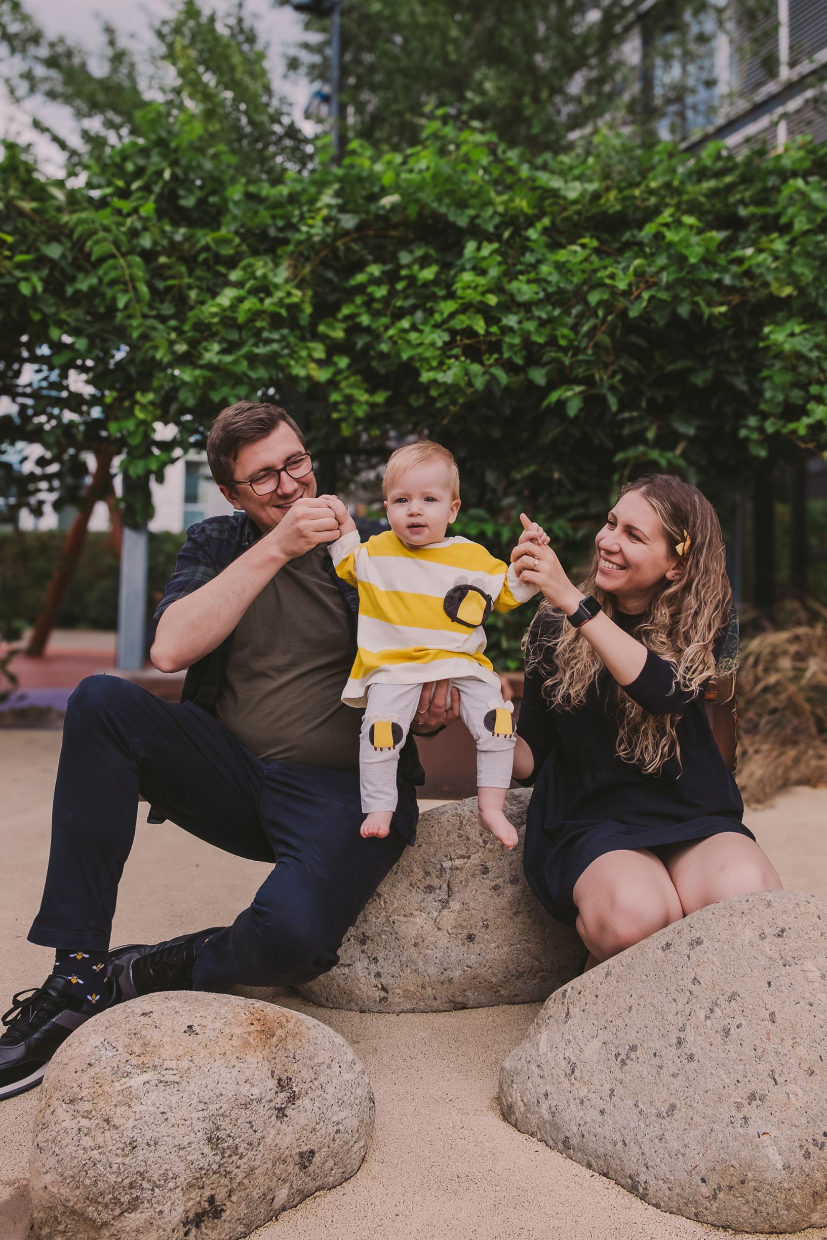 A series of candid family moments captured on large rocks in a garden setting showing playful interactions and laughter.