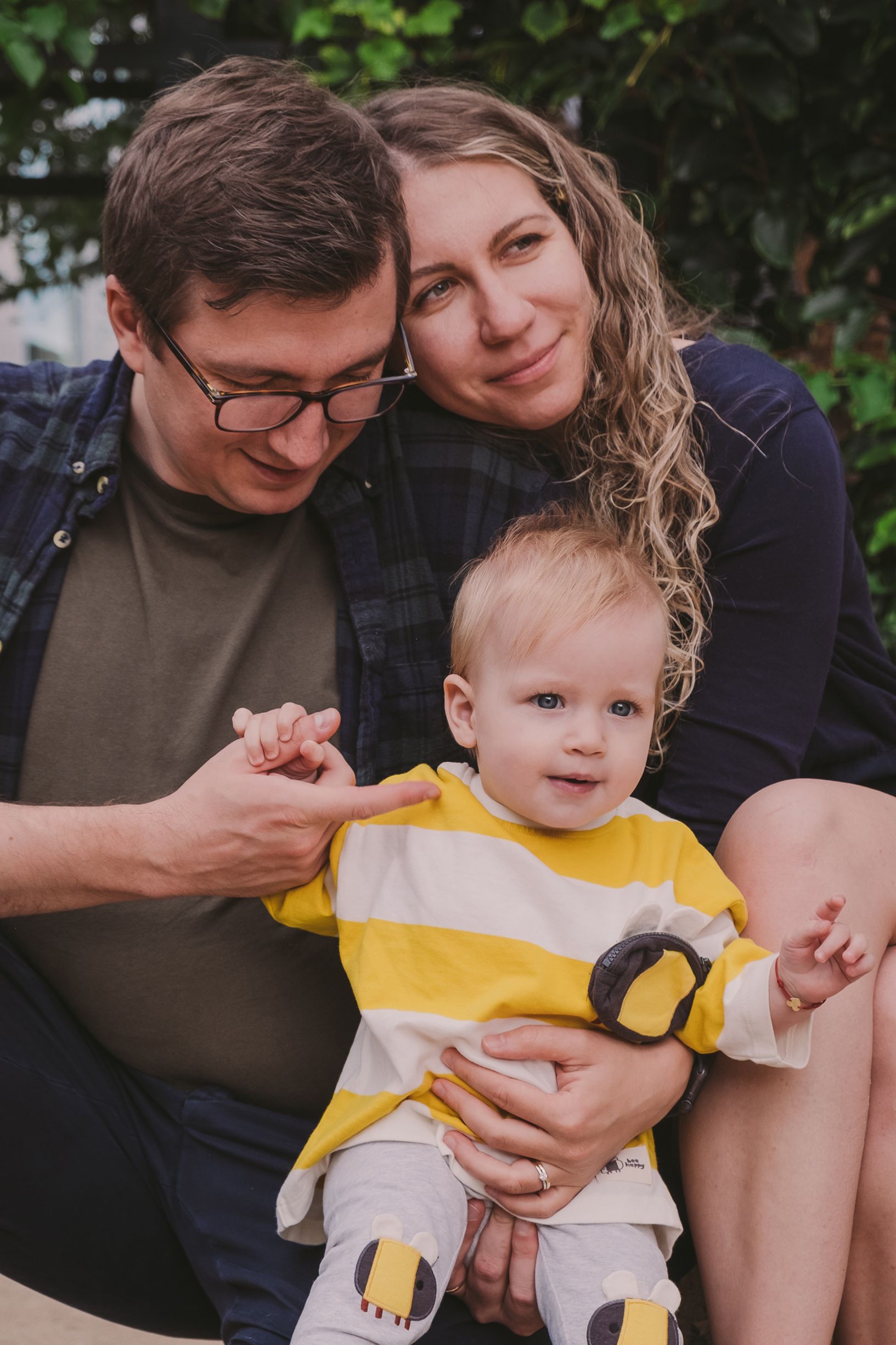 A tender family moment captured outdoors with a baby wearing a yellow outfit.