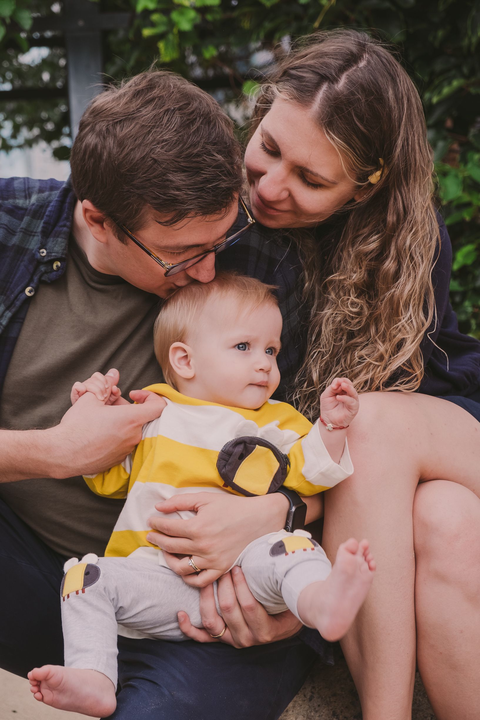 An intimate family portrait showing affectionate moments with a baby in yellow clothing.