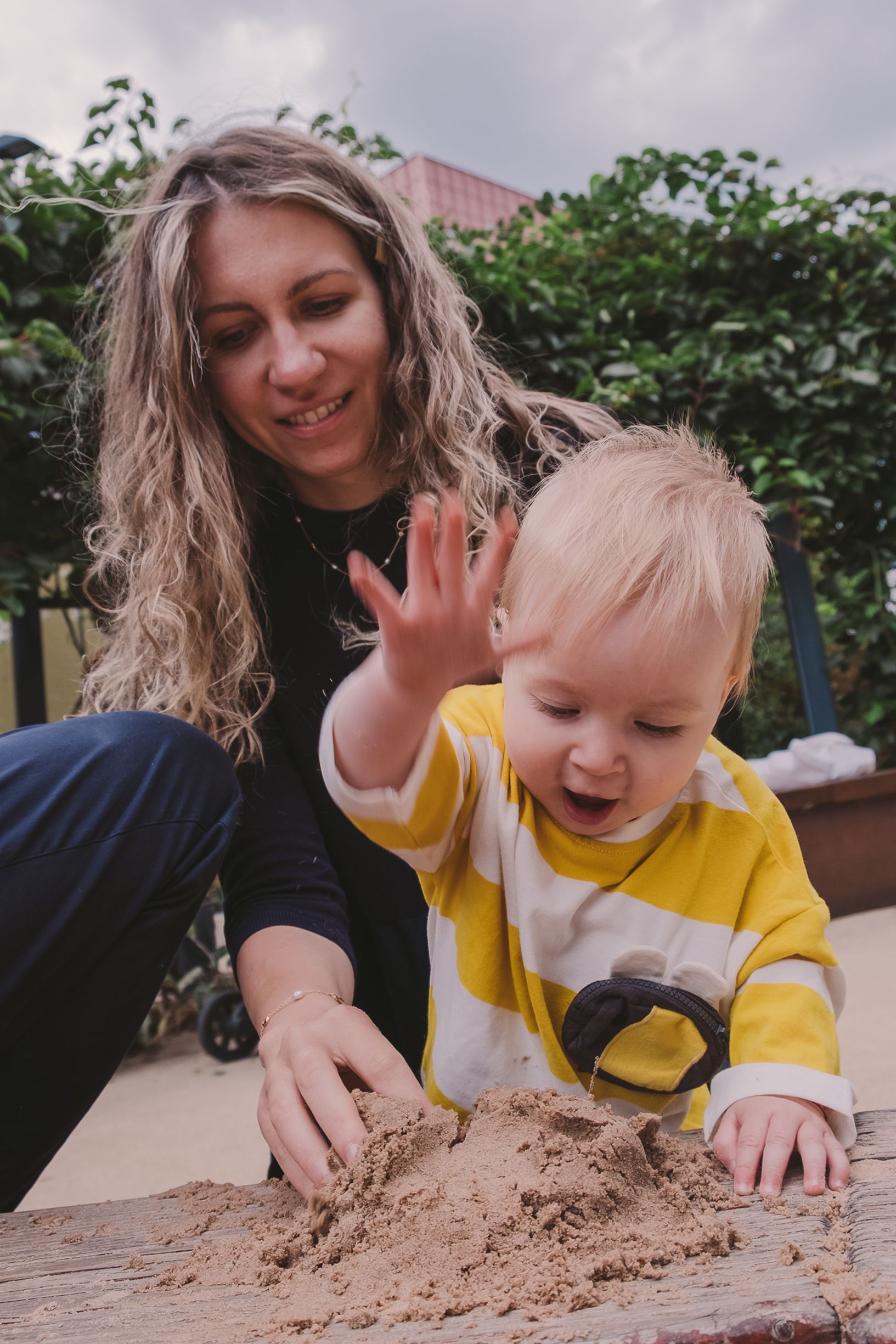 Parent and child playing together in sandbox with joyful expressions and natural interactions.