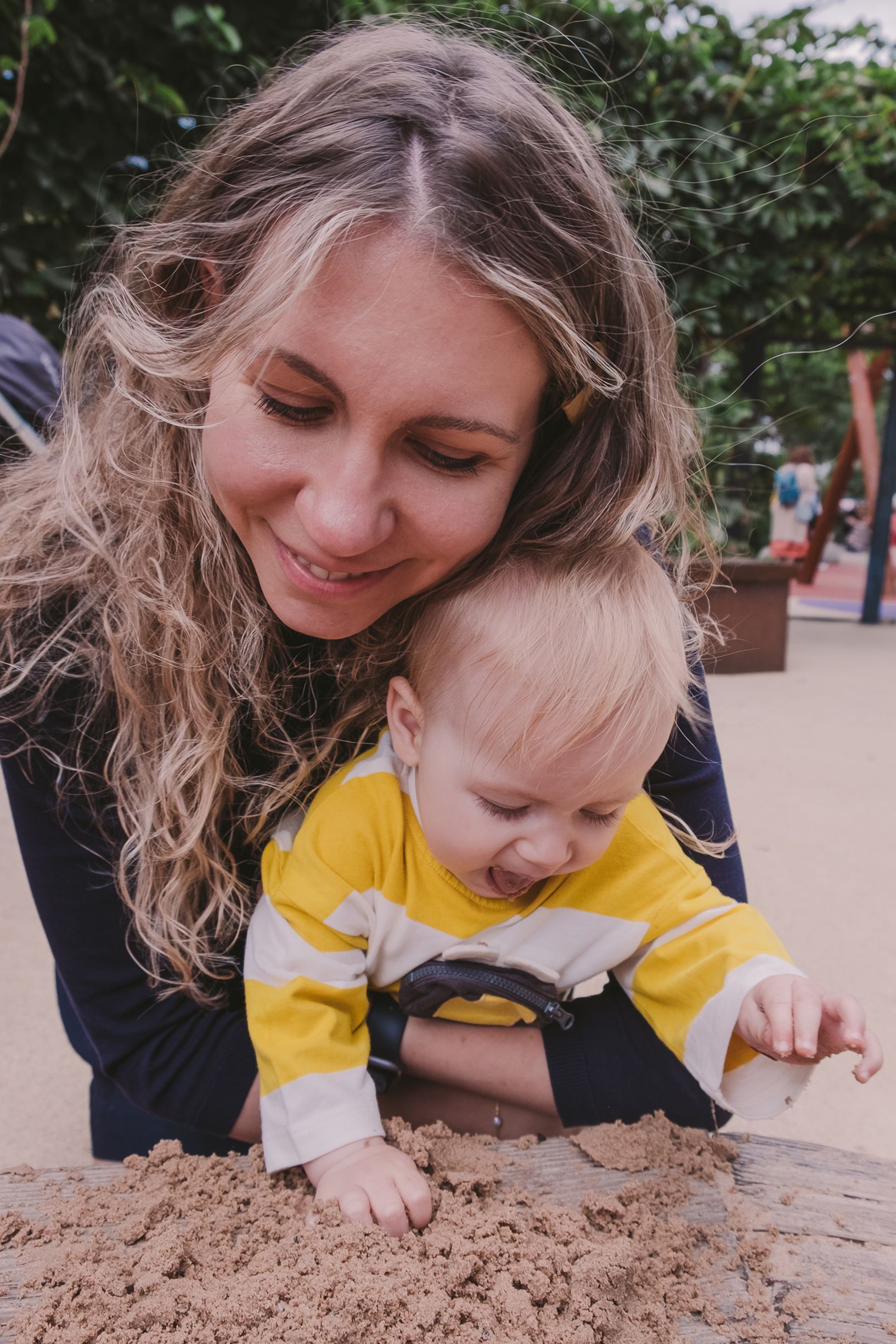 Parent and child lying on ground examining sand together in a series of candid outdoor moments.