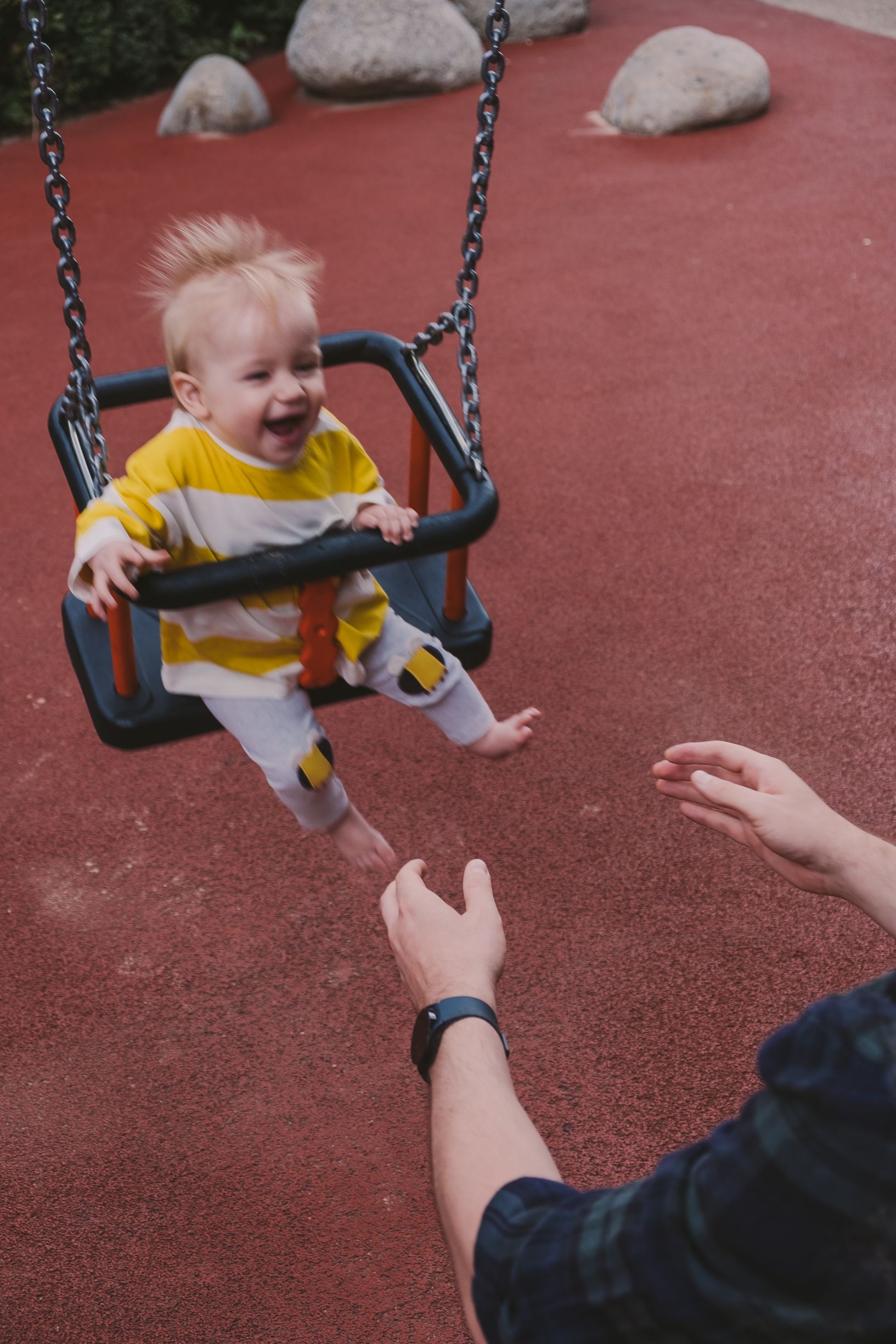 A child in yellow clothing enjoys swinging at a playground with helping hands nearby.