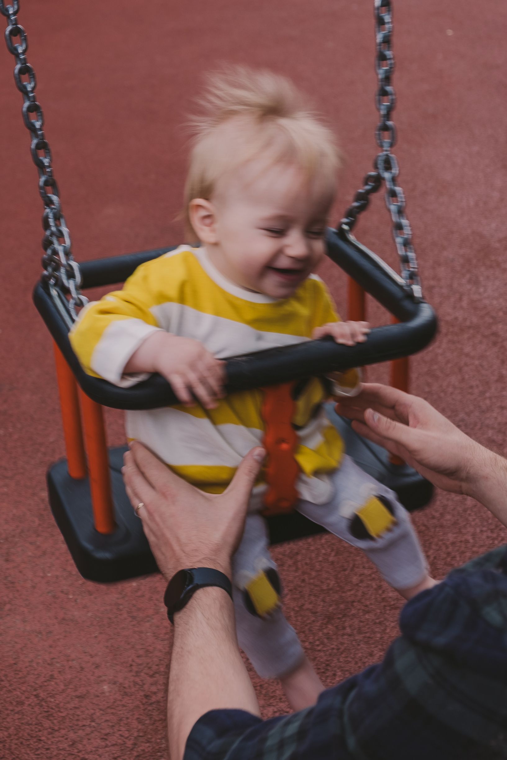 A child in a yellow shirt laughs while being pushed on a playground swing set.