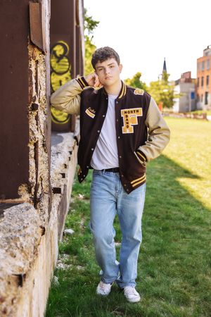 Multiple shots of someone posing near a wooden post wearing a varsity jacket and jeans in autumn sunlight.