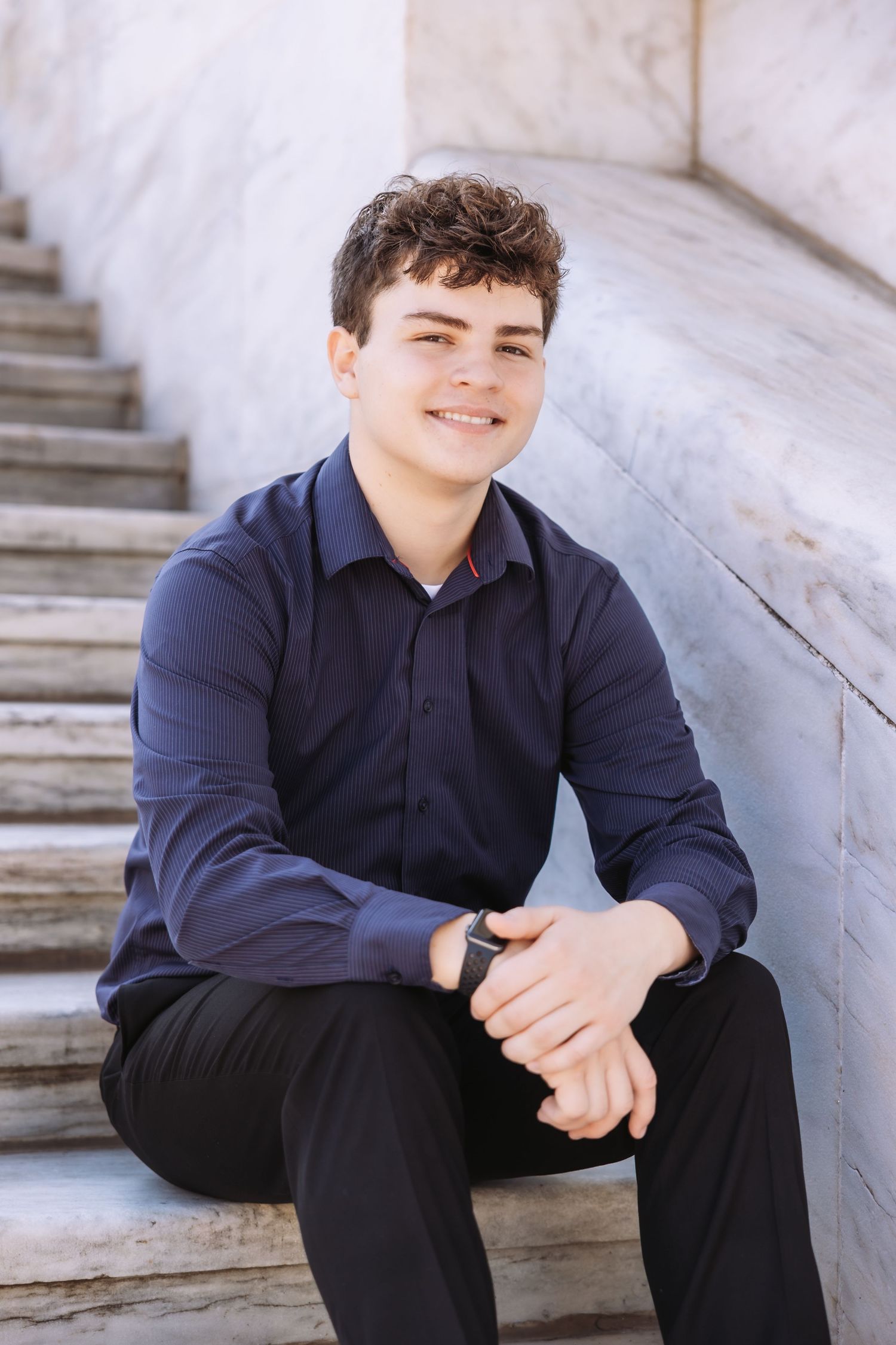 A person in a navy blue shirt sits casually on concrete steps in an outdoor setting.