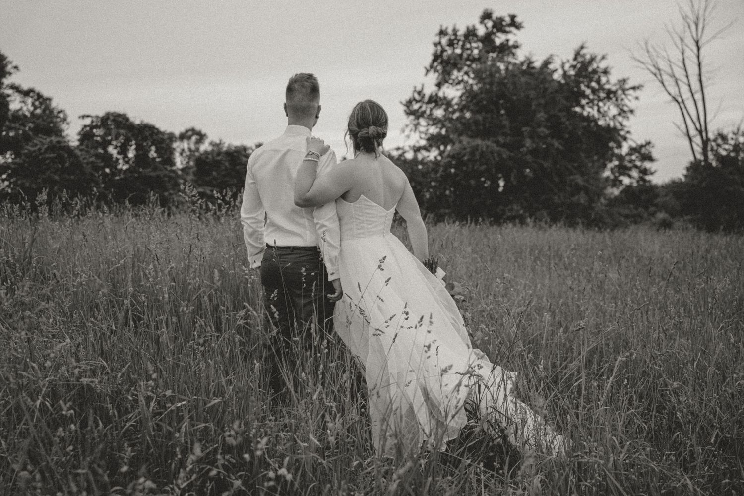 Couple sharing a warm embrace in a lush green meadow during golden hour engagement session.