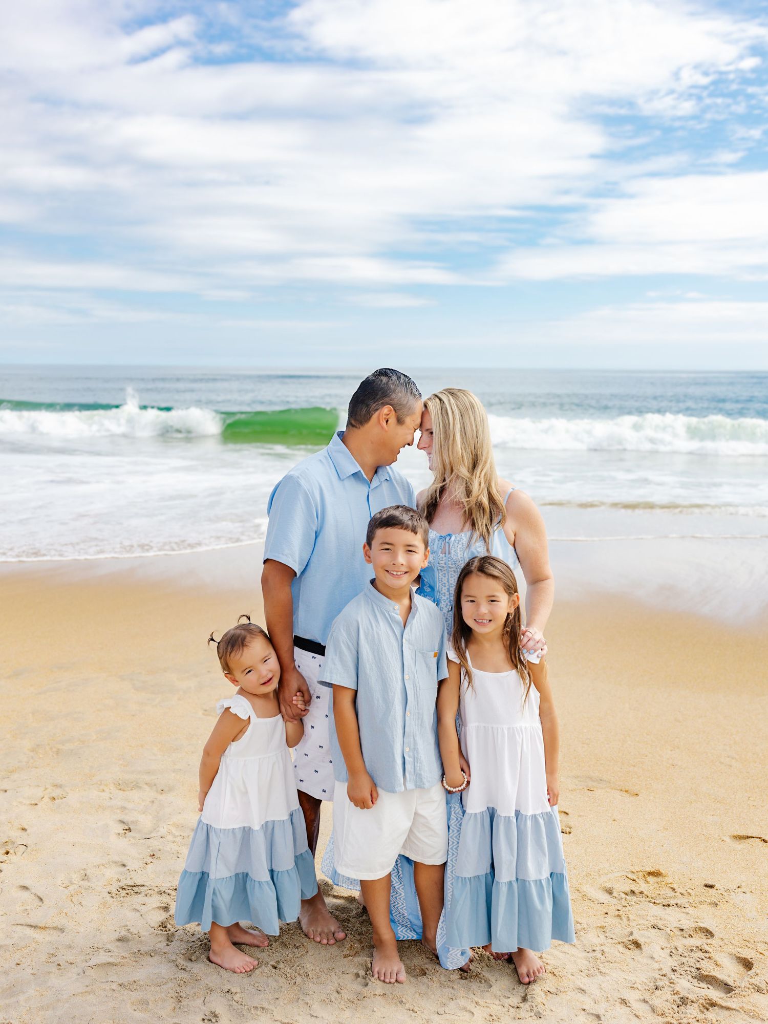 Family in coordinating blue and white outfits poses together on sunny beach.
