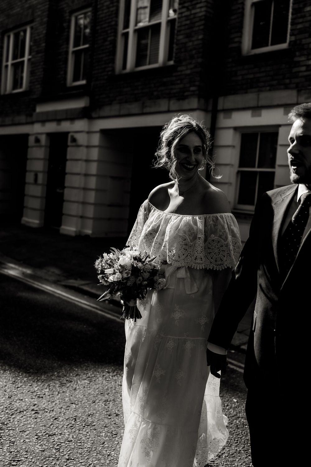 A black and white photo sequence showing a bride in a vintage-style lace wedding dress walking outside a brick building.