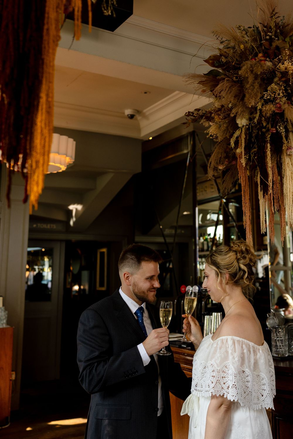 A couple toasts with champagne at a wedding reception in an elegant venue with decorative floral arrangements.
