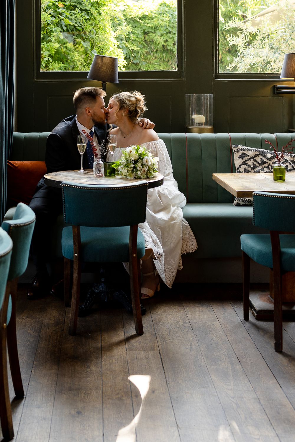 A restaurant interior with blue booth seating and wooden tables next to large windows with garden views.