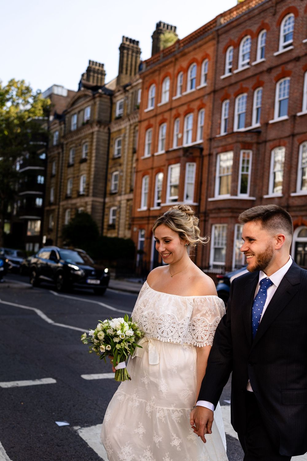 Newlyweds pose together on a charming street lined with classic red brick buildings.
