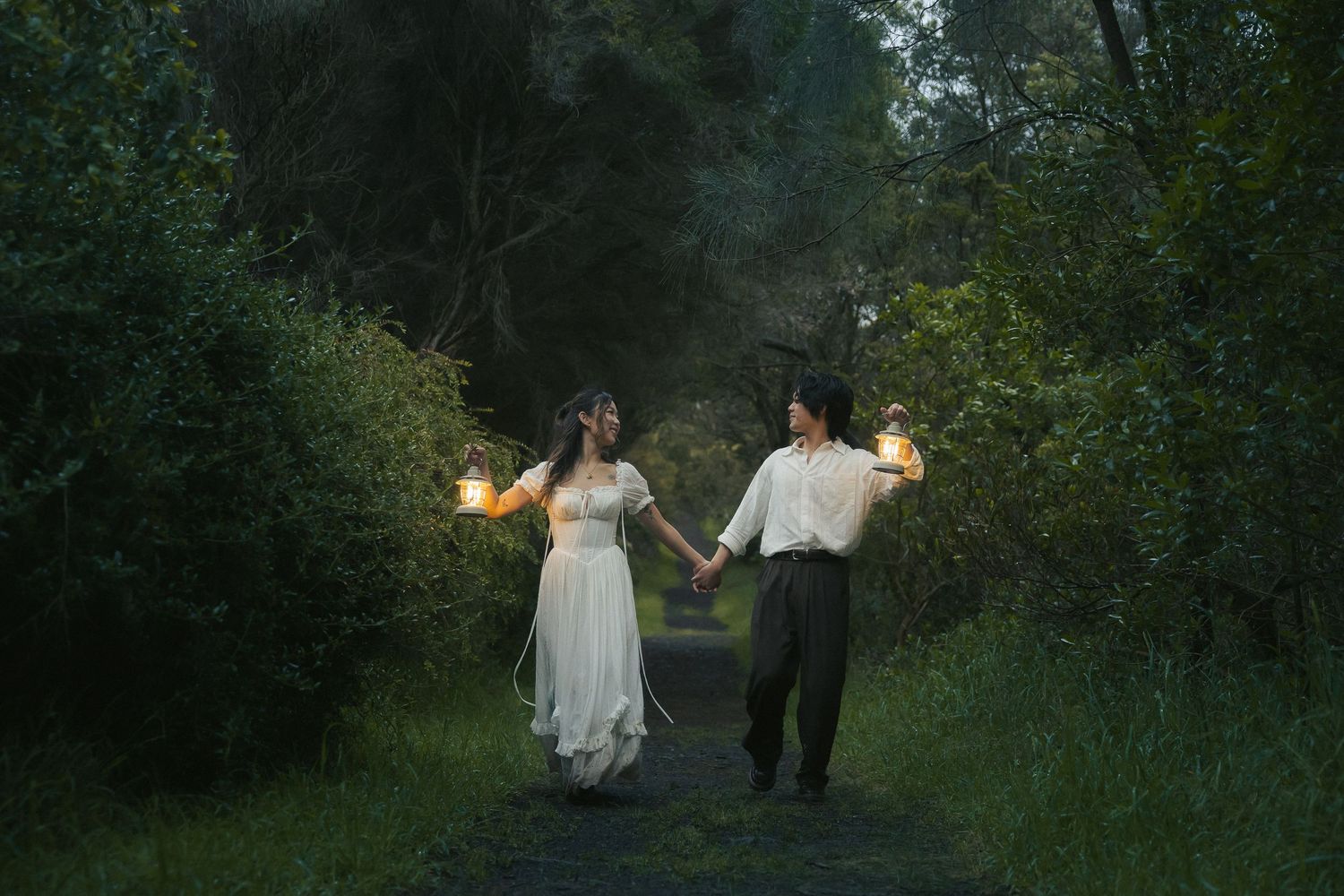 A white dress glows ethereally among dark trees on a moody forest path at dusk.