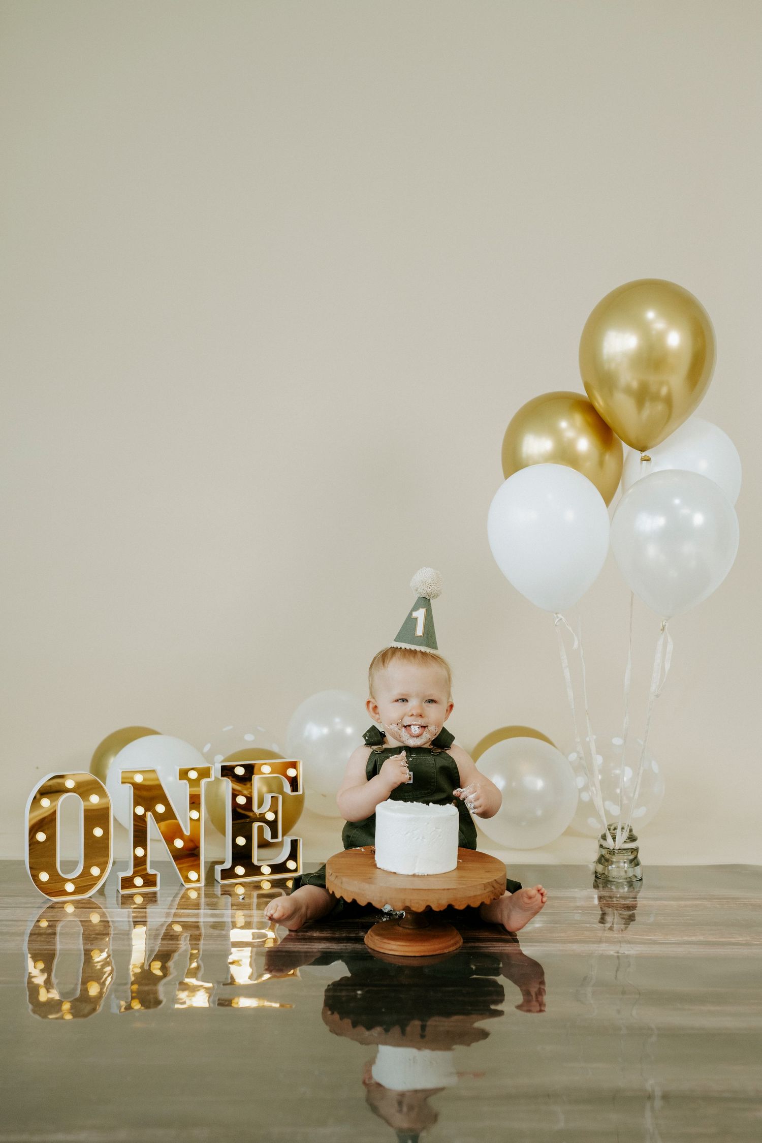 Festive first birthday scene with gold and white decor, cake, and reflective floor setup.