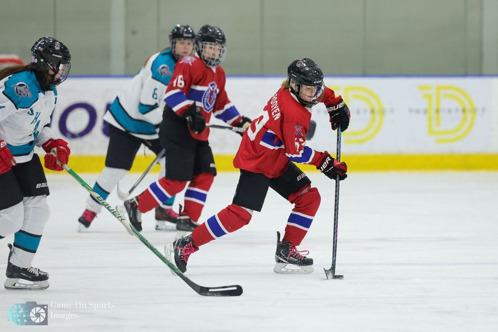 Hockey players in red and teal jerseys battle for the puck during an intense game on the ice.