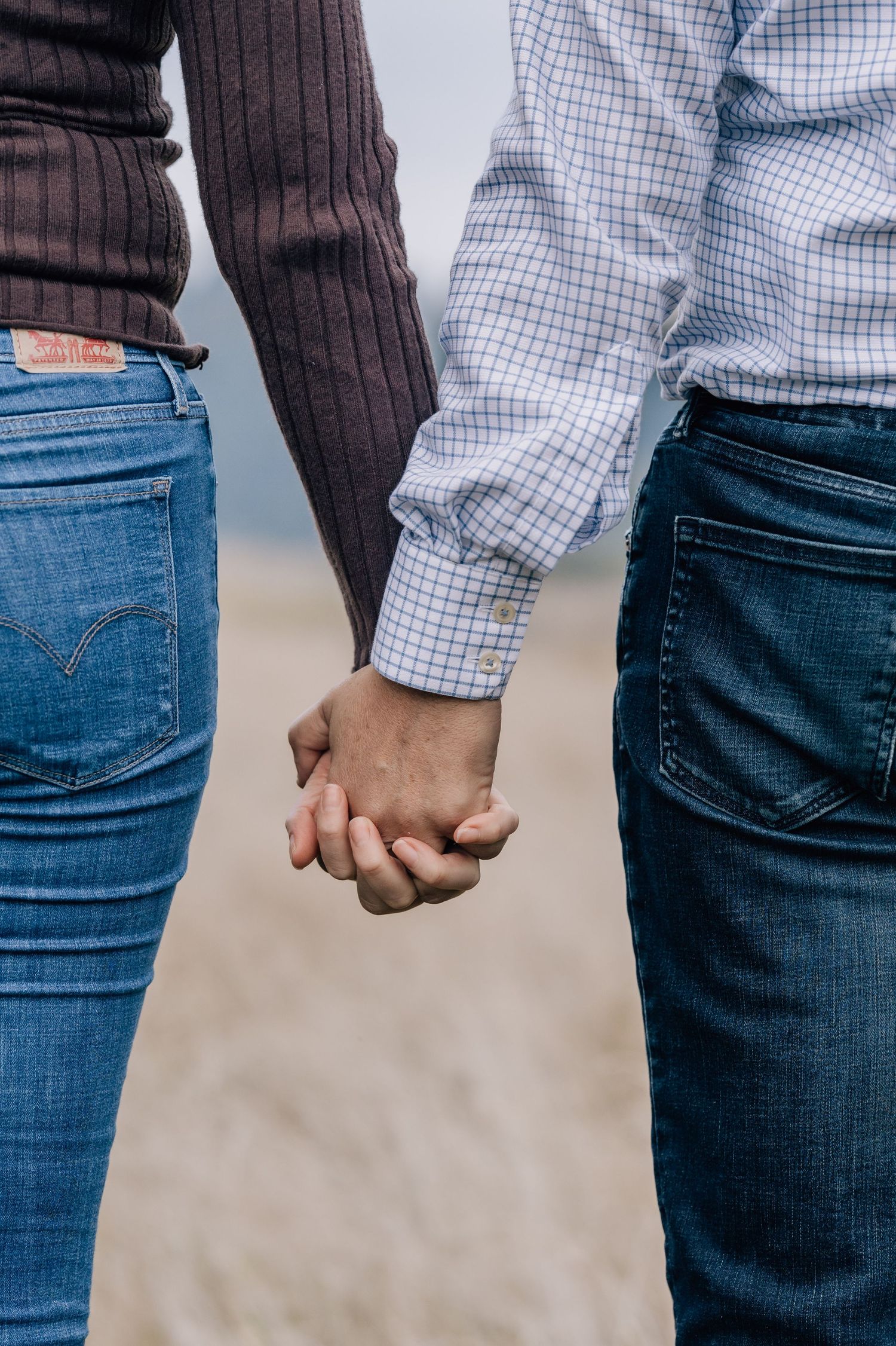 Close-up of a couple holding hands wearing jeans in an outdoor field setting.