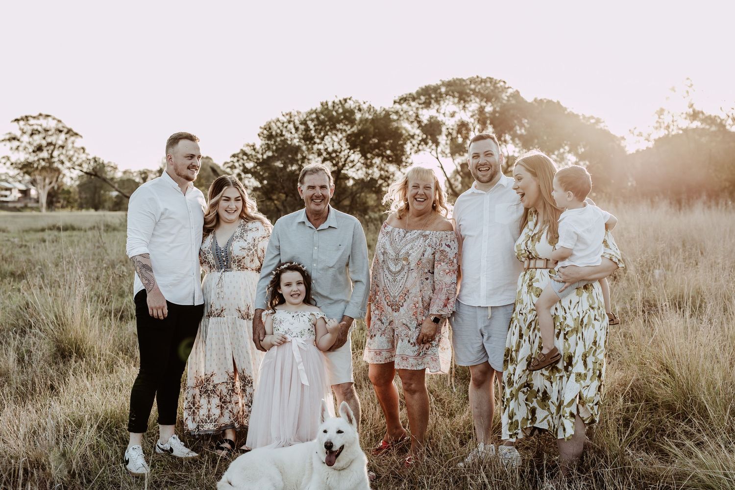 Extended family gathering in a field during golden hour wearing coordinated outfits.