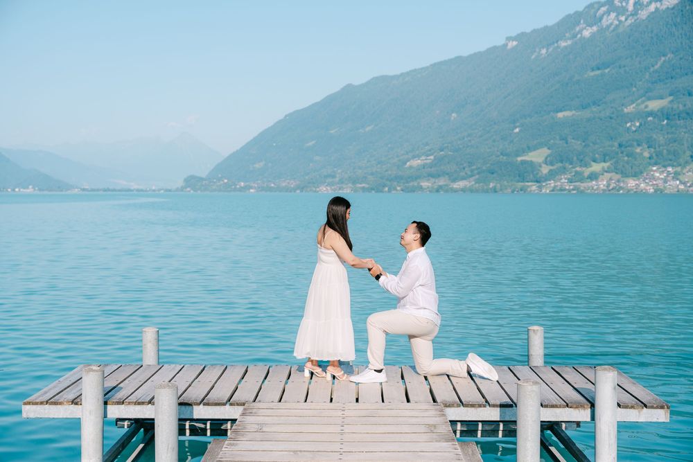 Two people share a romantic moment on a wooden dock in Iseltwald overlooking a scenic mountain lake.