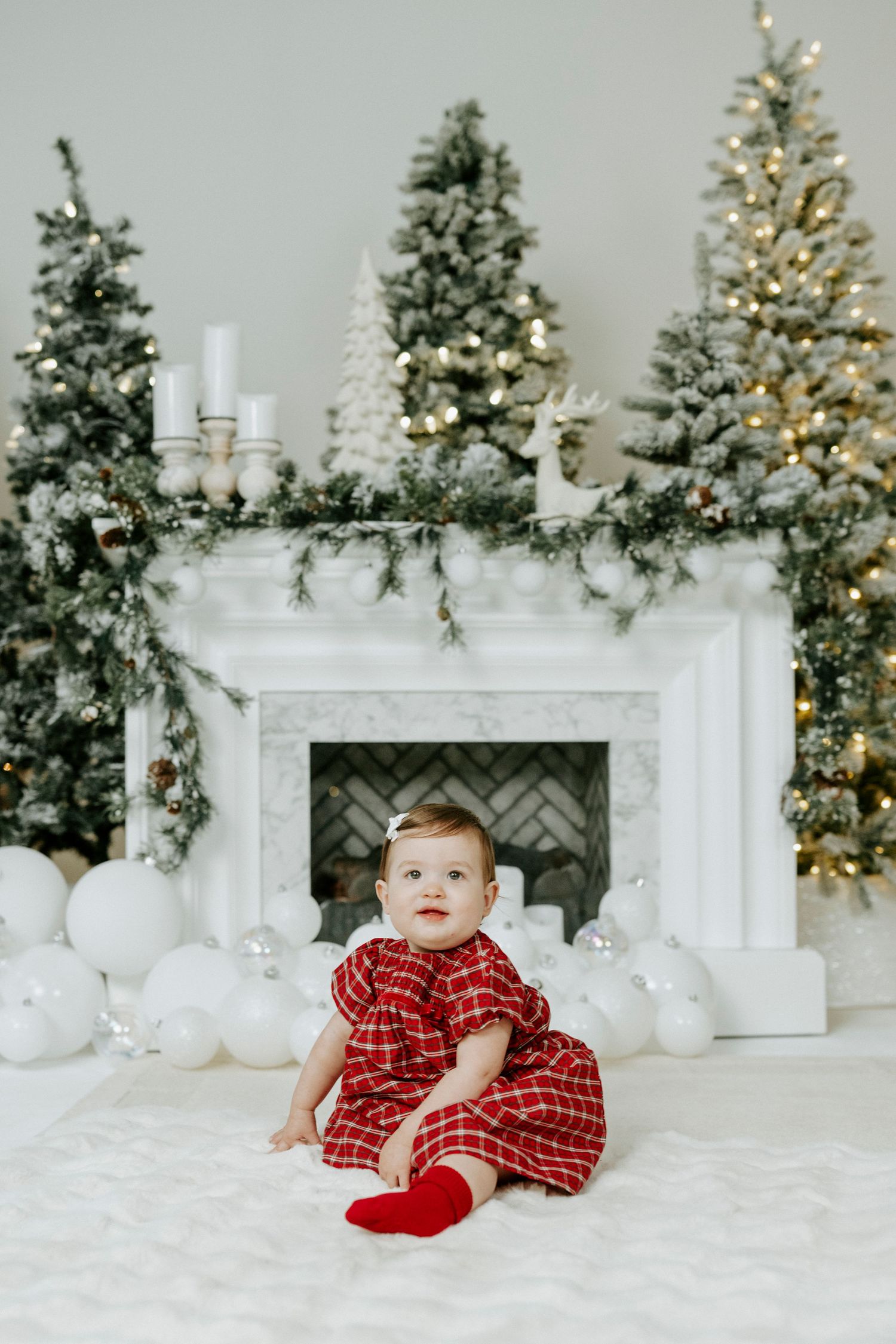 Holiday scene with decorated Christmas trees, white fireplace mantel, and festive decorations in a bright studio setting.