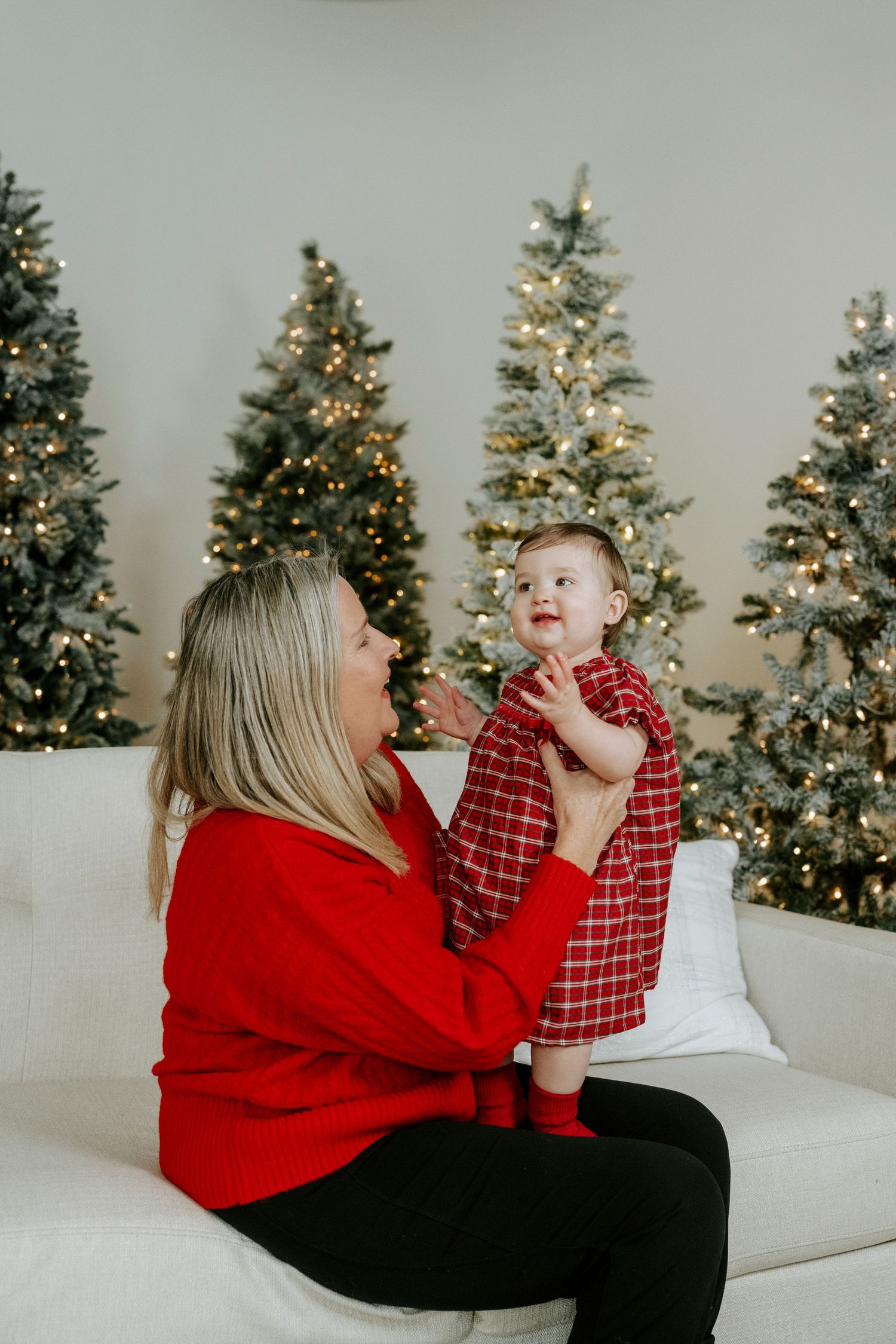 A heartwarming holiday scene with matching red outfits sitting on a white couch with decorated Christmas trees in background.
