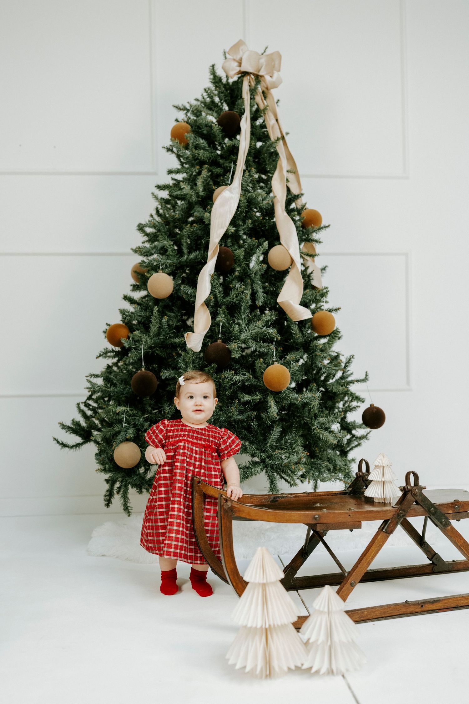 Four connected photos of a rustic Christmas scene with a decorated evergreen tree, wooden sled, and holiday decor against white.