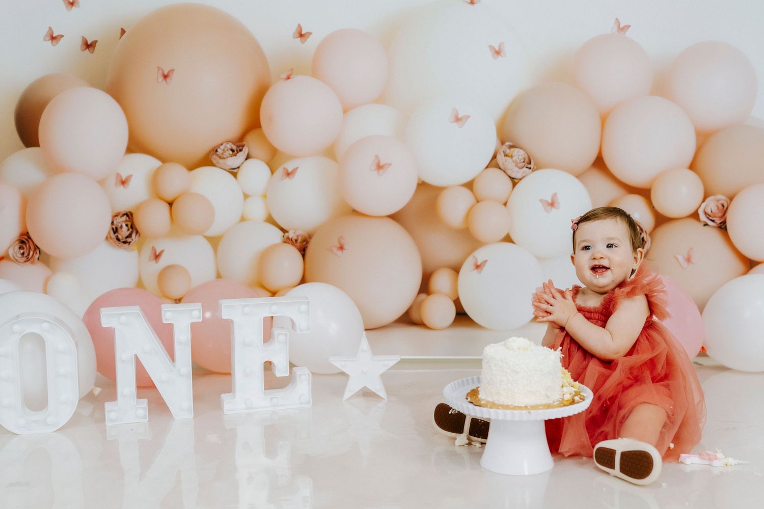 Collage of first birthday party photos with peach balloons, cake, and decorations in soft pastel tones.