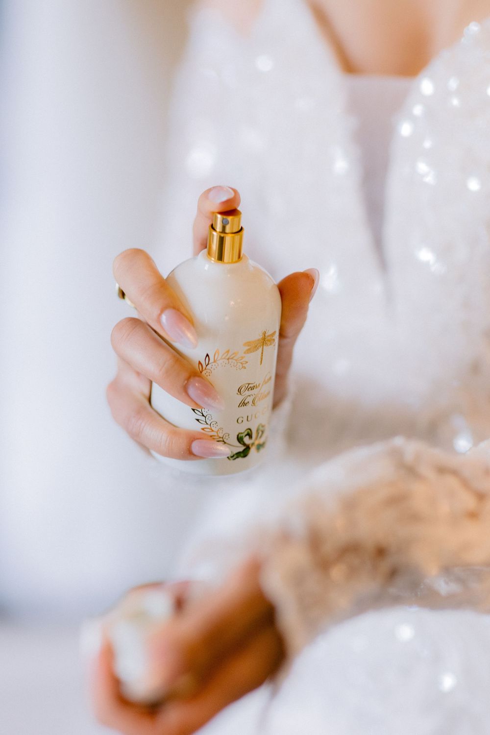 Elegant gold perfume bottle being held against soft white fabric with delicate bokeh light effects in the background.