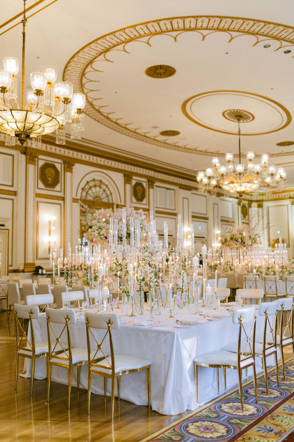 Elegant ballroom with crystal chandeliers, ornate gold ceiling details, and white-clothed tables set for a formal reception.