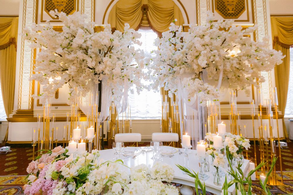 Elegant wedding reception hall decorated with crystal chandeliers, white floral arrangements and golden drapes.