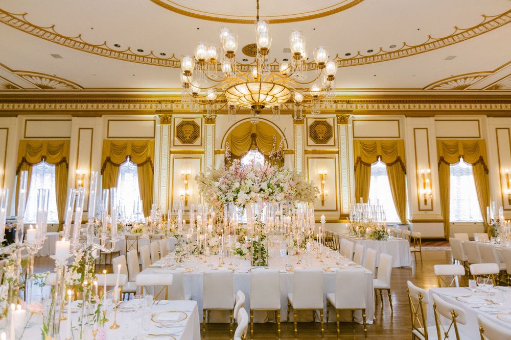Elegant ballroom with ornate gold trim, crystal chandeliers and white-clothed round tables set for a formal reception.