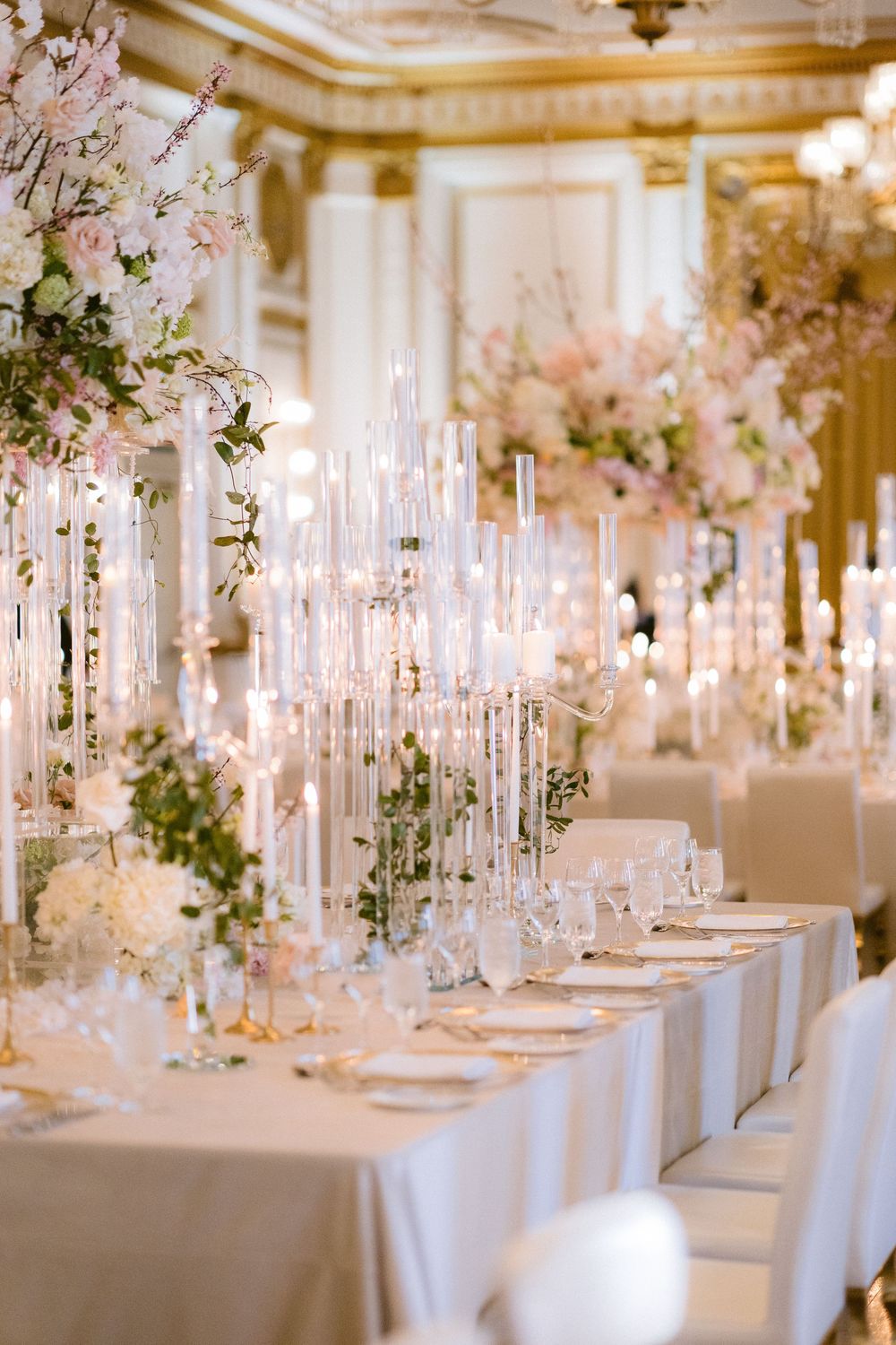 Elegant wedding reception tables decorated with tall white candles and pink floral arrangements in an ornate ballroom setting.
