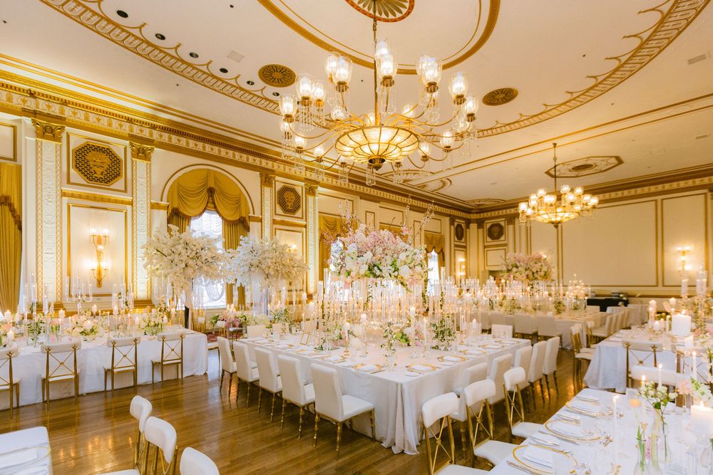 Elegant ballroom set for a wedding reception with crystal chandeliers, ornate gold ceiling details and white table settings.
