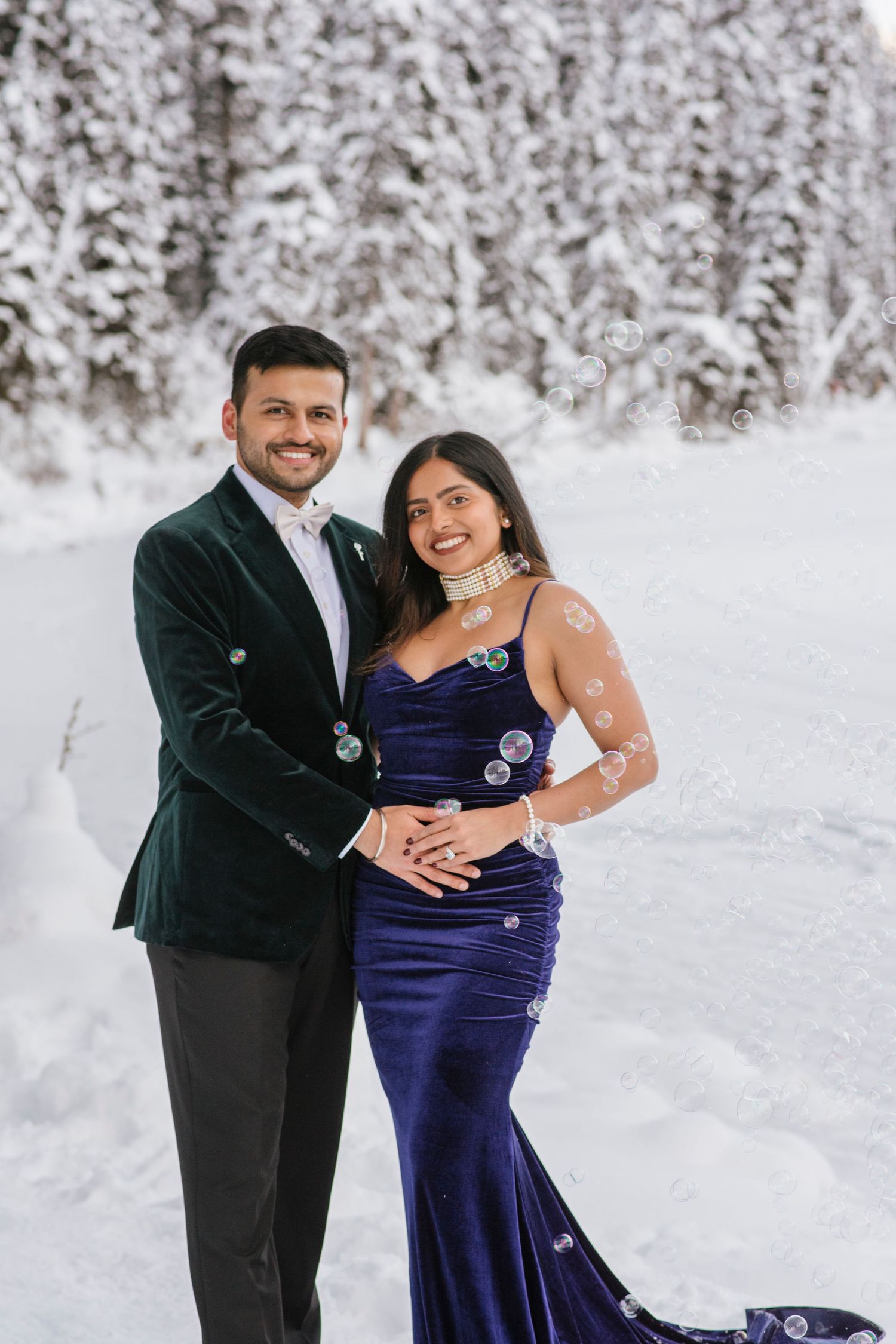 Romantic winter couple portraits on Lake Louise shoreline with soft snow and mountains behind. Surrounded by bubbles.