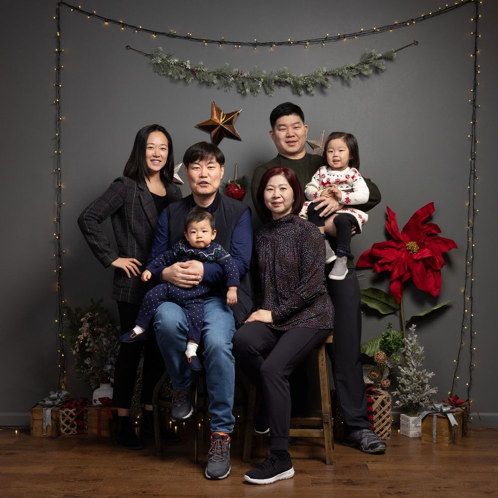 A family sits together on a wooden bench for holiday photos with festive poinsettia and garland decorations.