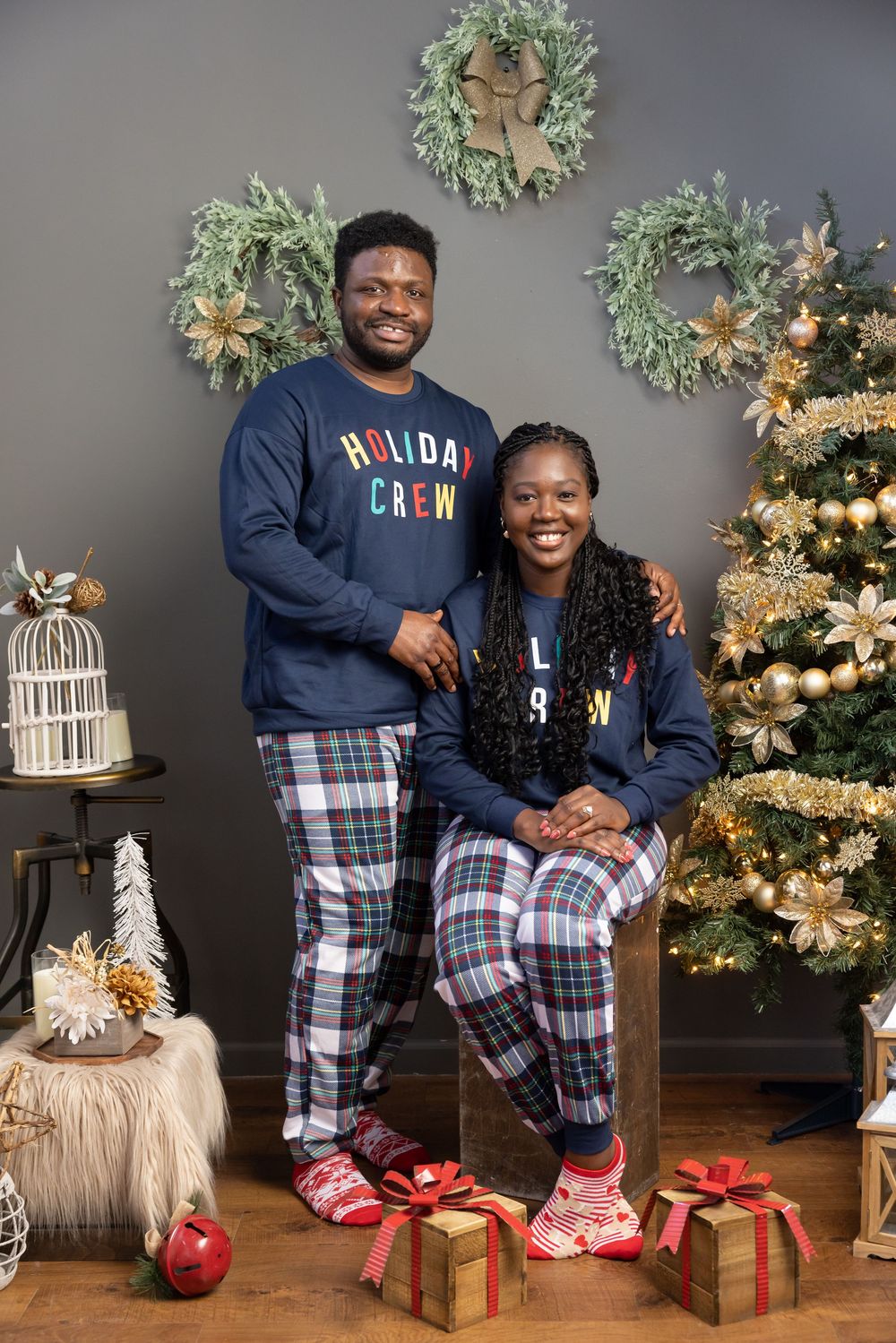 A festive holiday scene with matching plaid pajamas, Christmas wreaths, decorated tree, and wrapped presents by the fireplace.