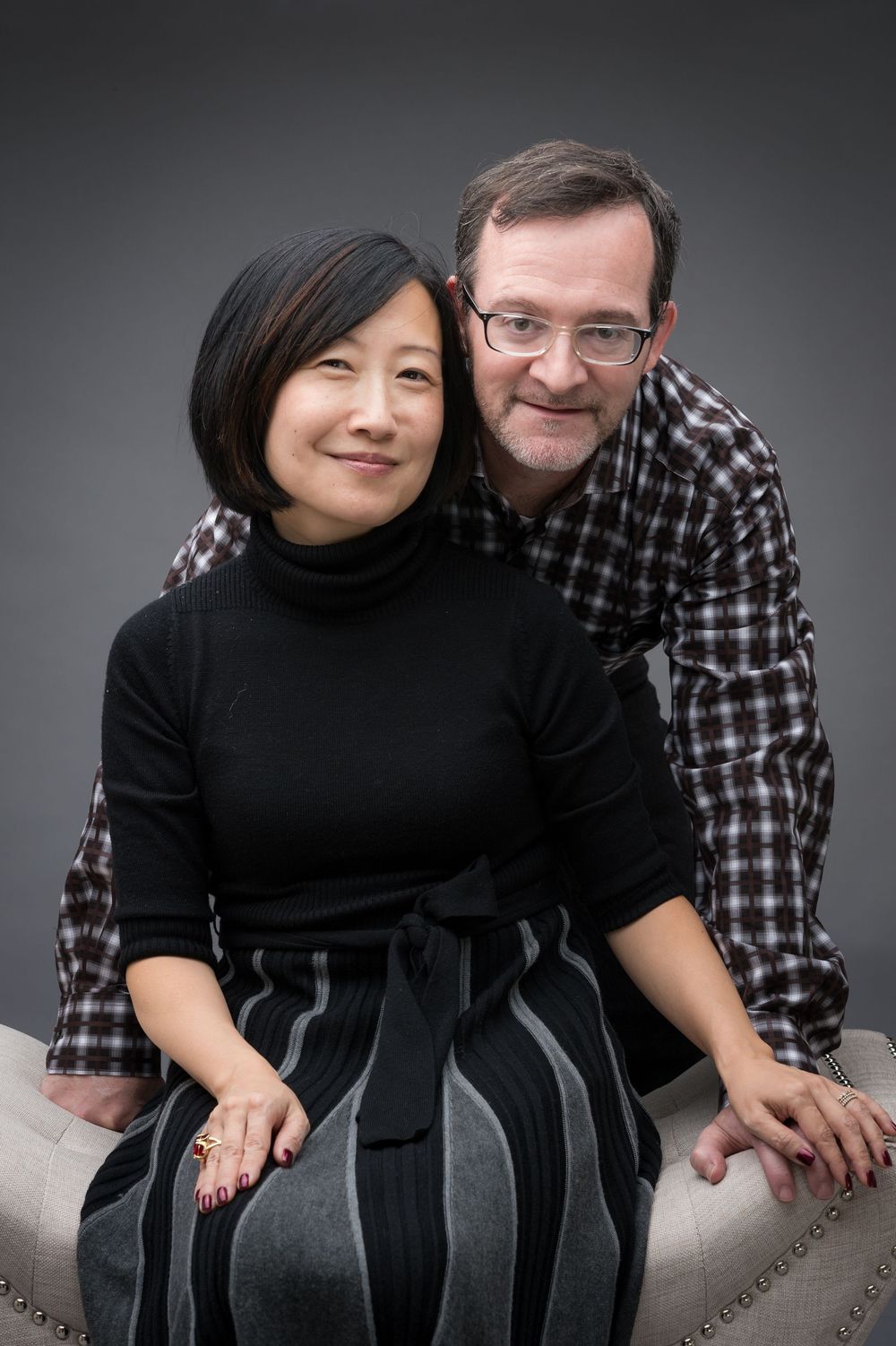A couple in black and plaid shirts poses together in a series of intimate portrait shots against a gray backdrop.