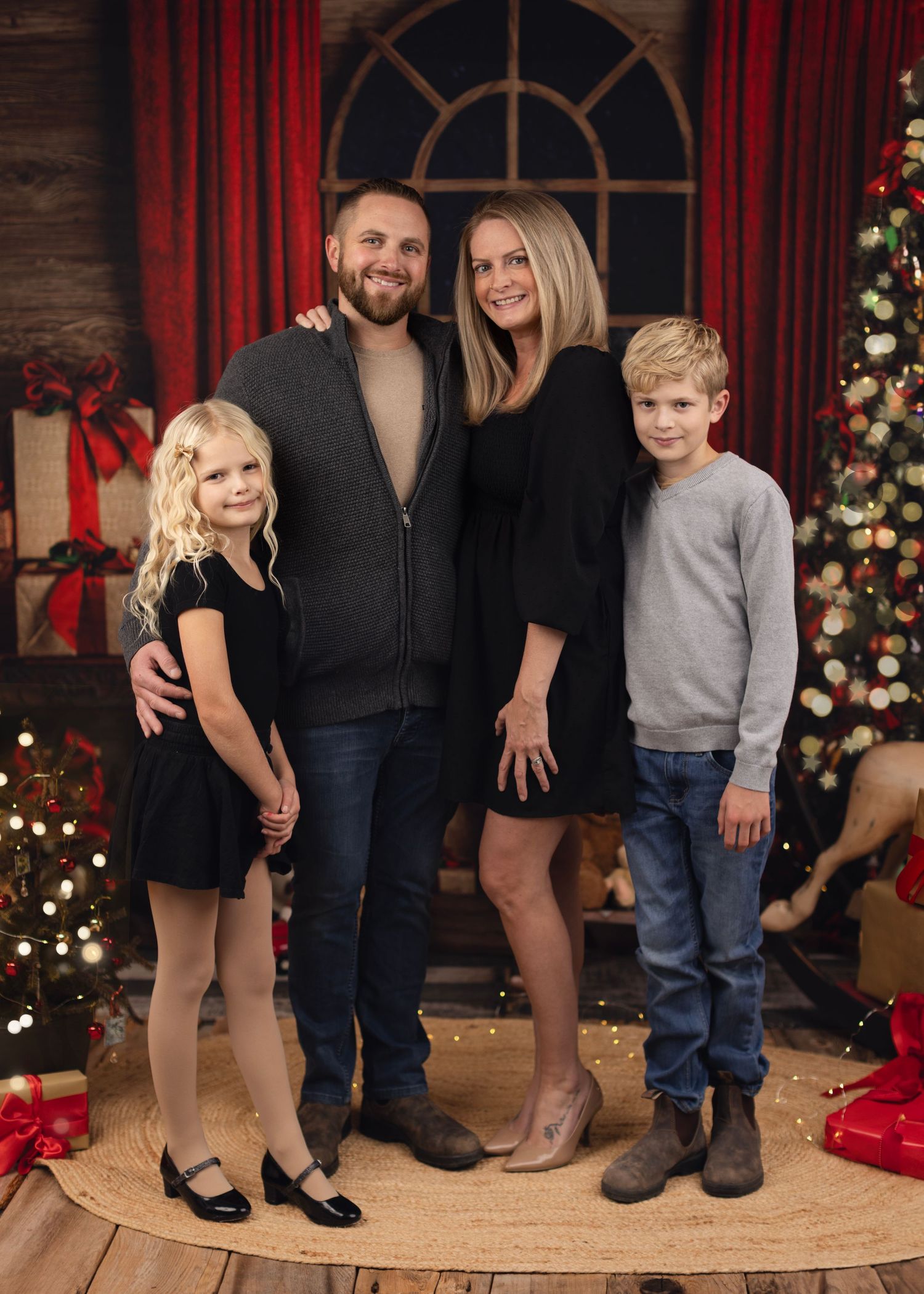 A family poses together for holiday photos in front of a decorated Christmas tree and rustic backdrop.