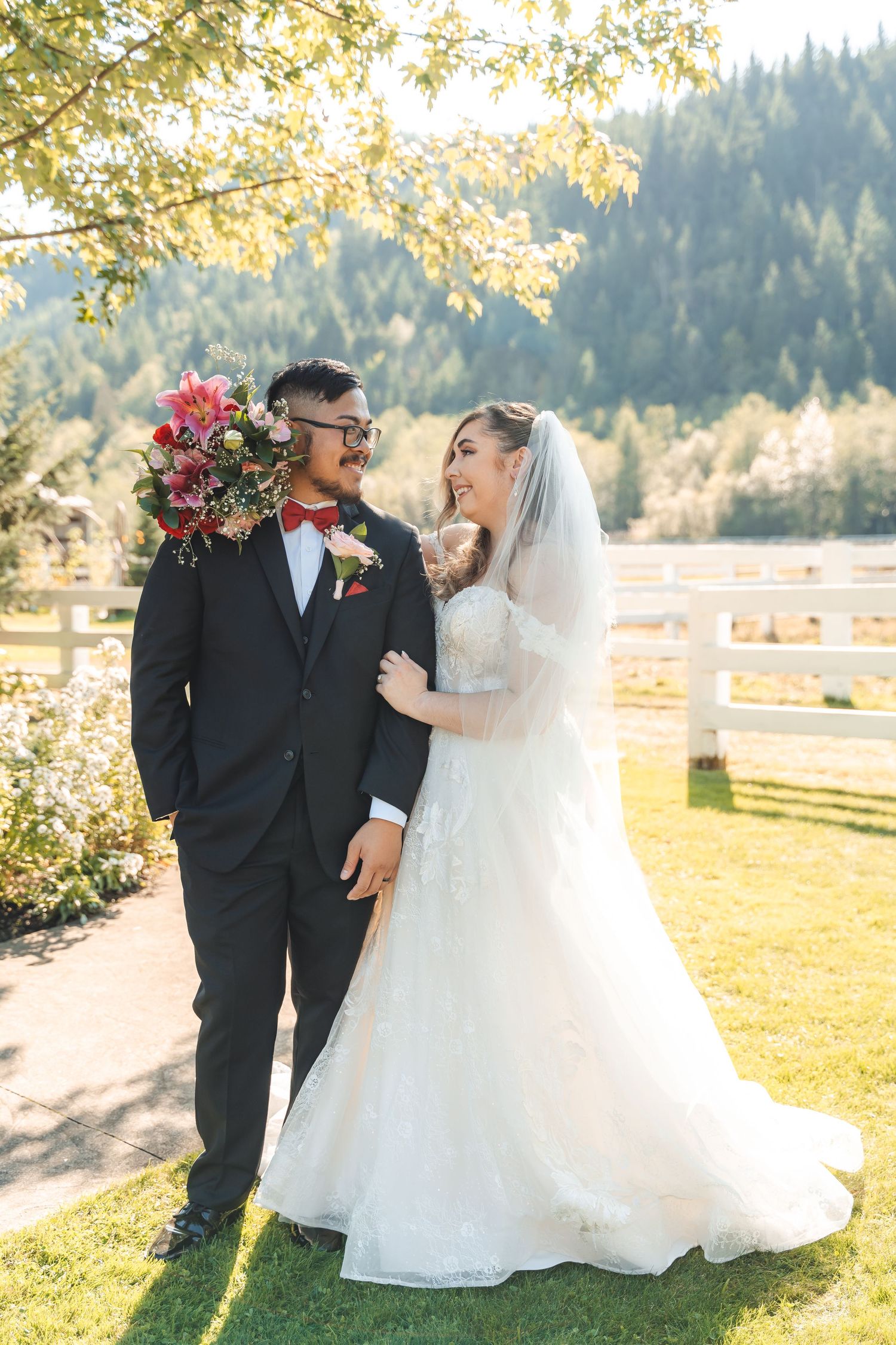 A romantic outdoor wedding photo of a couple sharing a joyful moment on a sunny day with mountains in the background.