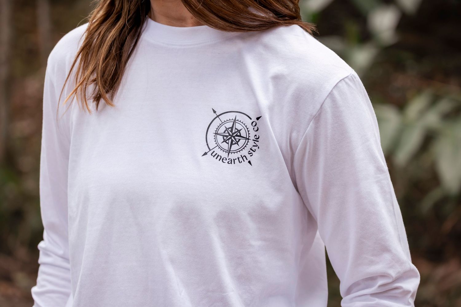Close-up of white long sleeve t-shirt with small embroidered logo detail.