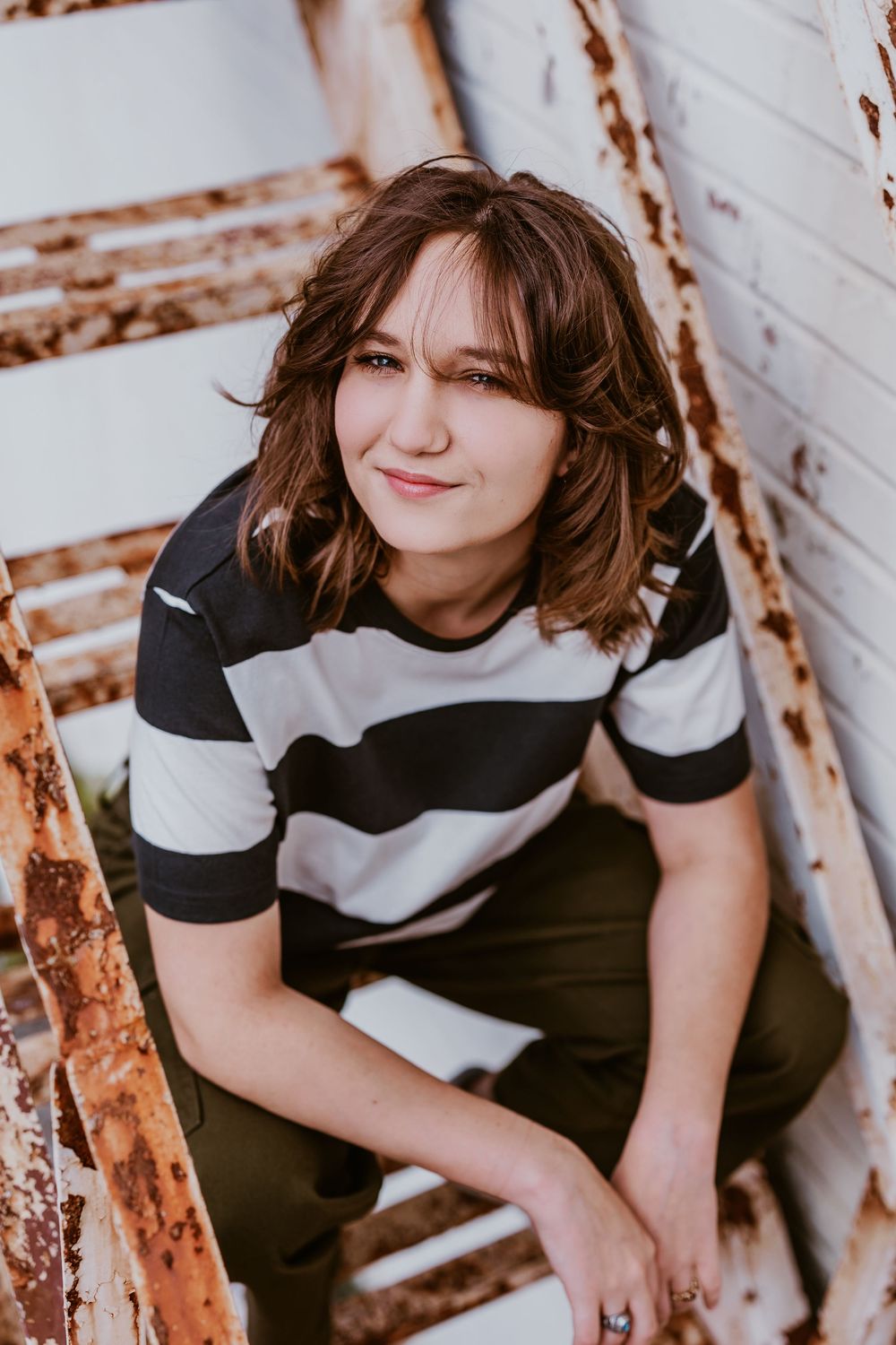 Artistic portraits against white brick wall wearing black and white striped shirt.