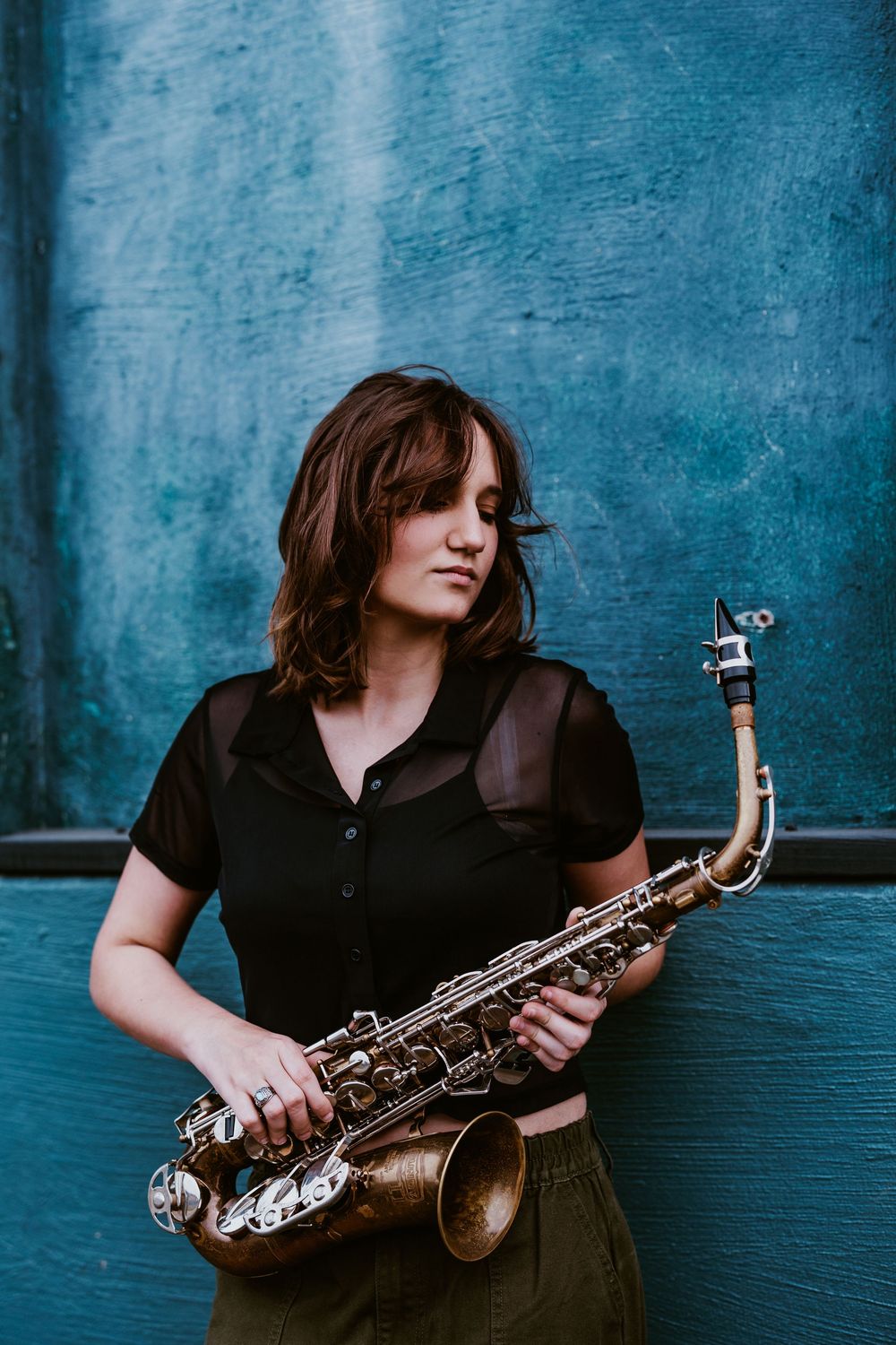 Musician poses with saxophone against blue wall in artistic photoshoot.