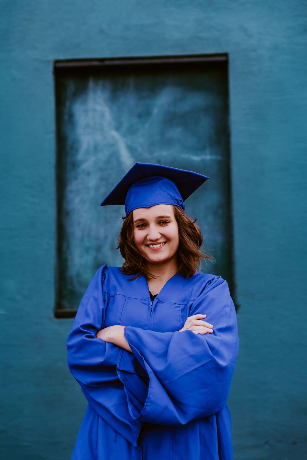 Graduate portrait series featuring someone in bright blue cap and gown against a blue wall backdrop.