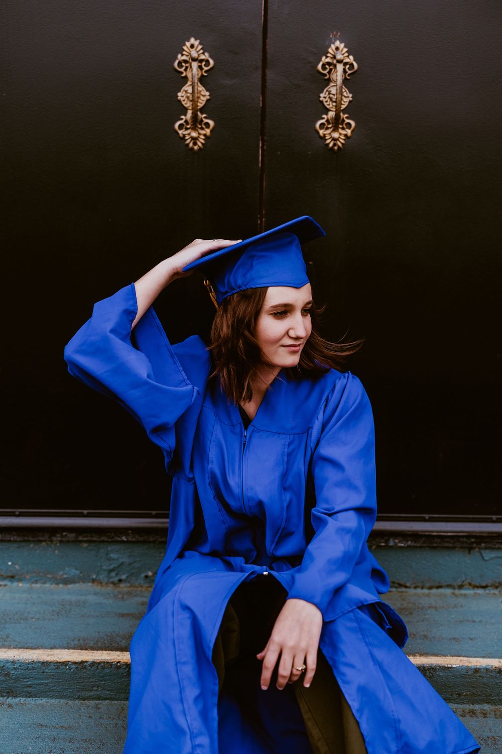 Graduation photos of someone in blue regalia posing on steps with decorative wall elements.
