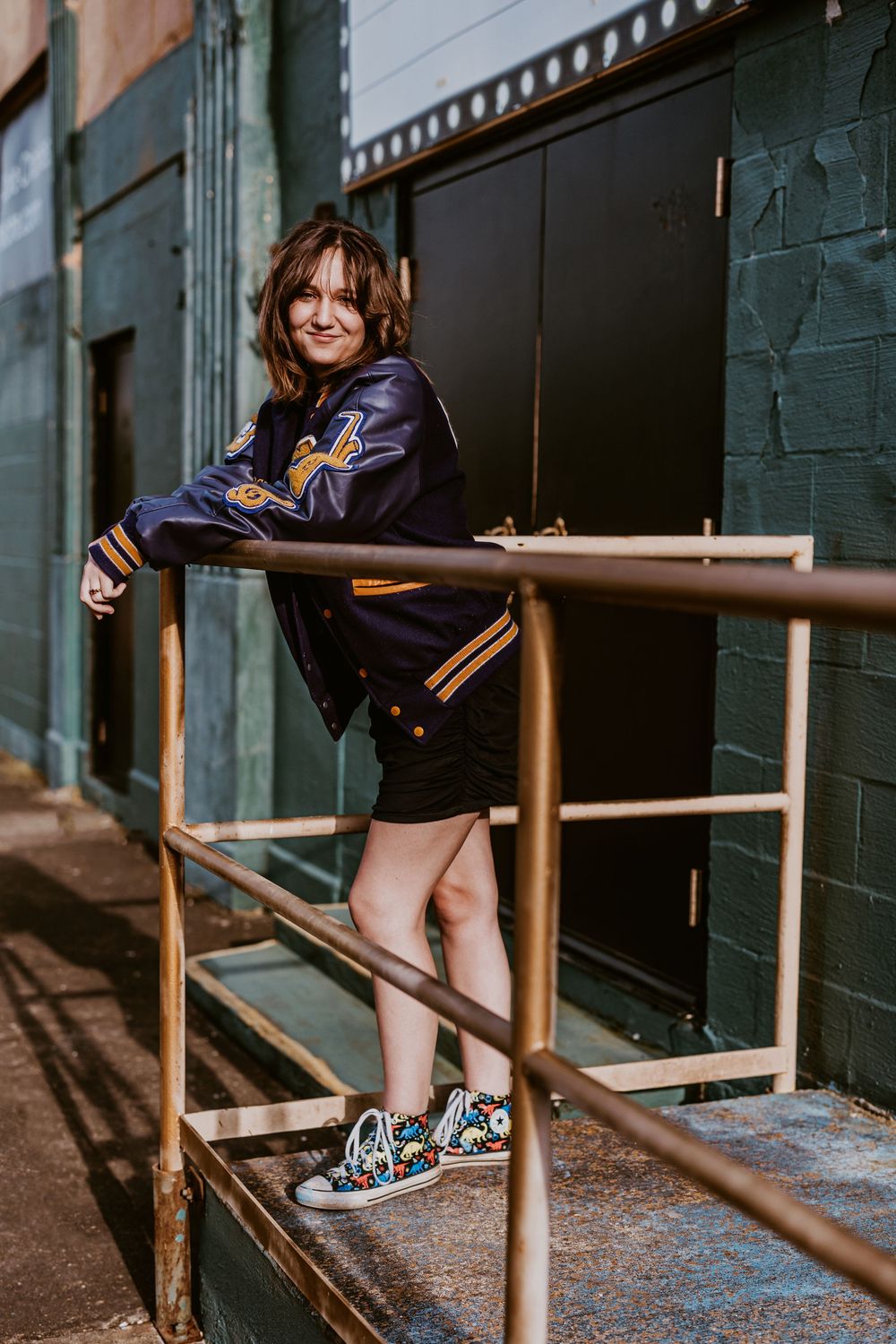 Someone in casual attire sitting on metal railings outside a brick building.