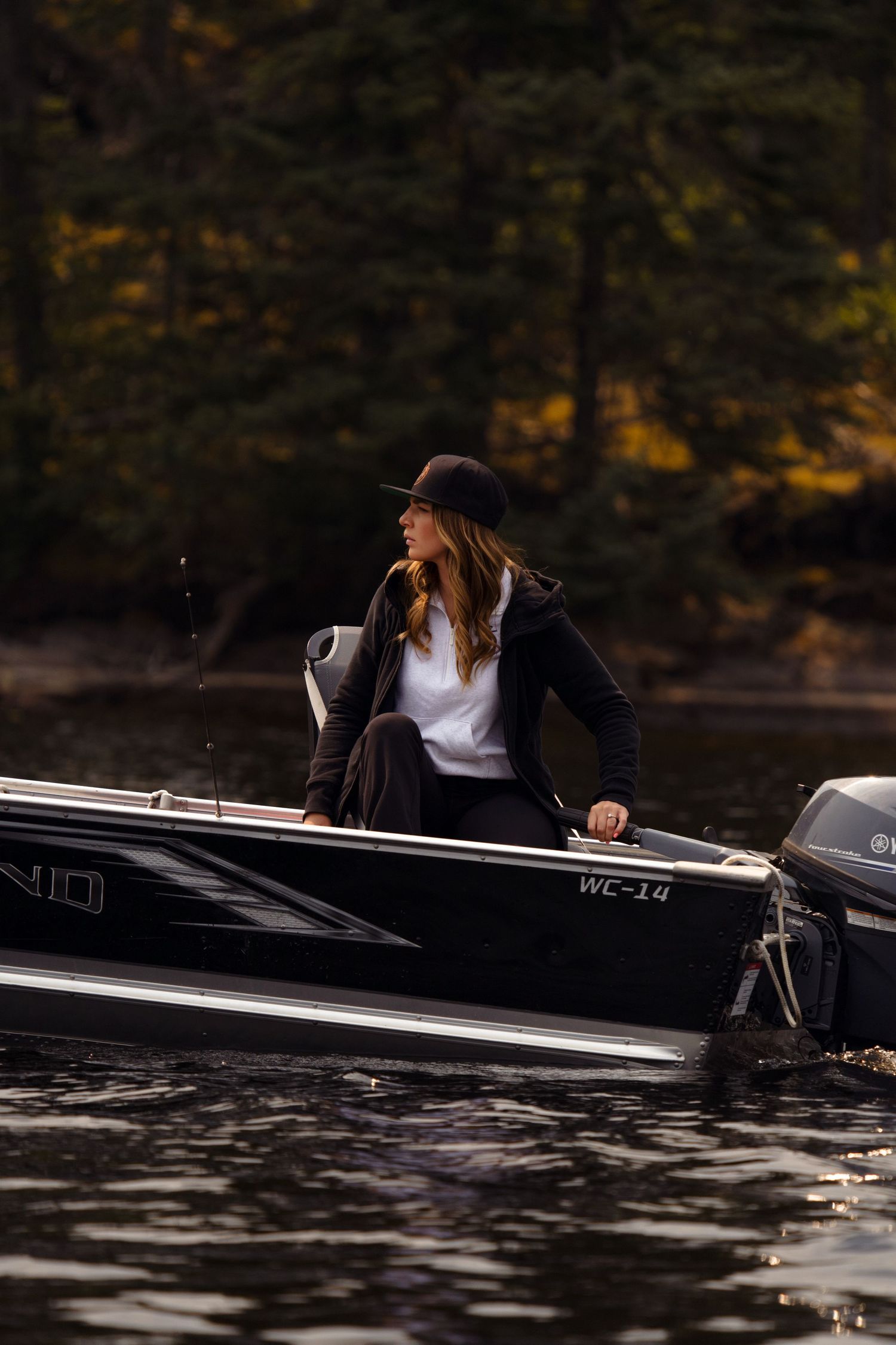 Black canoe gliding across dark waters with fall foliage in the background.